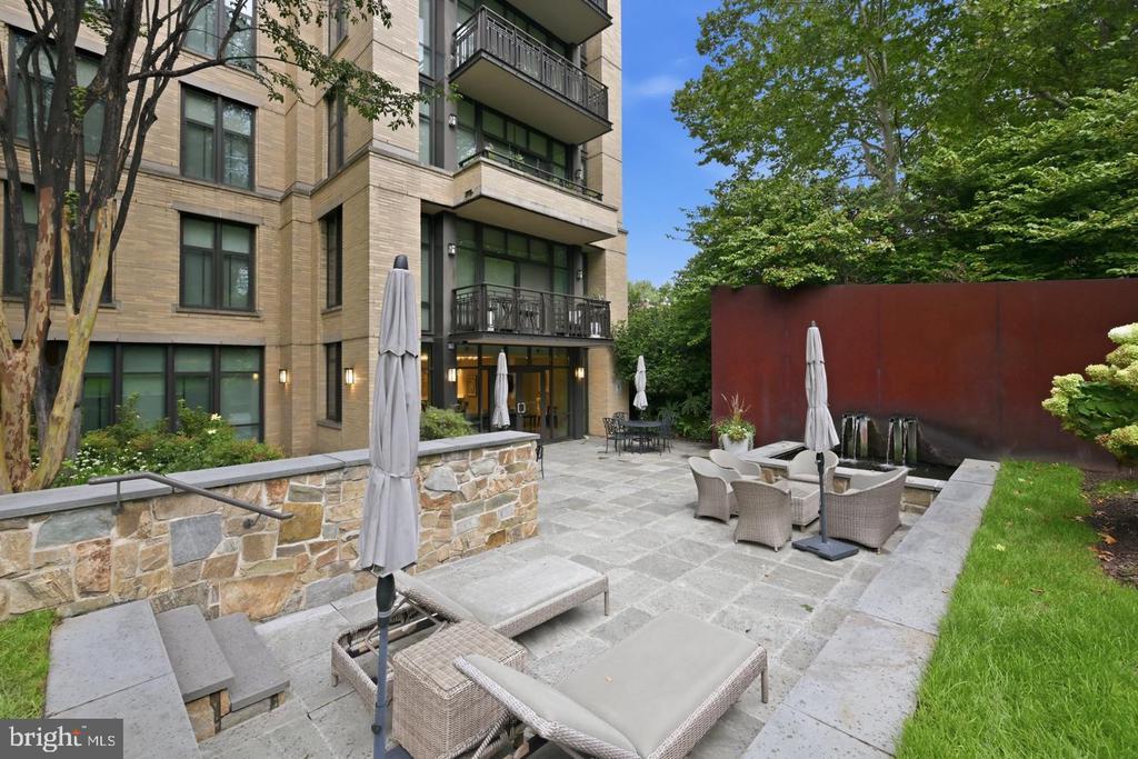 Residential courtyard patio with wicker seating, closed umbrellas, and stone paving beside the building.