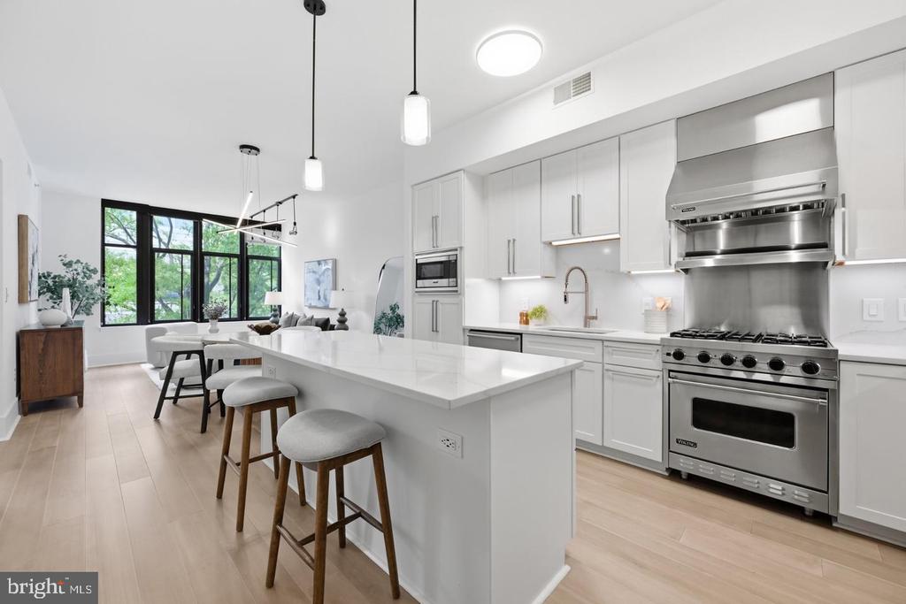 Open-plan kitchen with a large island, three stools, and stainless steel range beneath a wide hood.