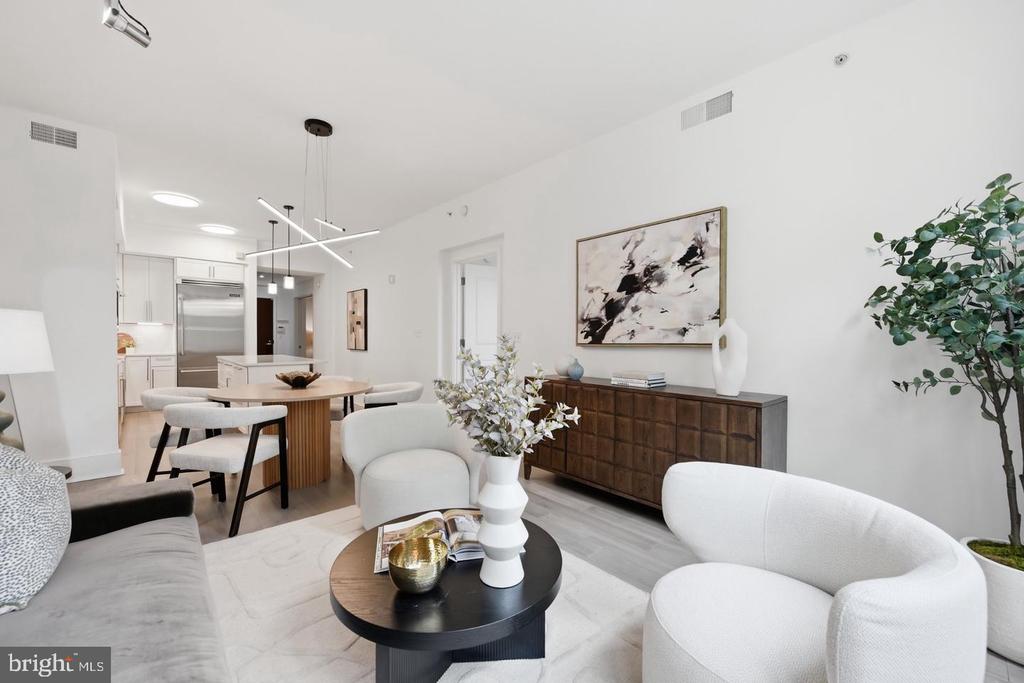 Staged living room with white curved seating, a dark wood sideboard, and an adjoining kitchen.