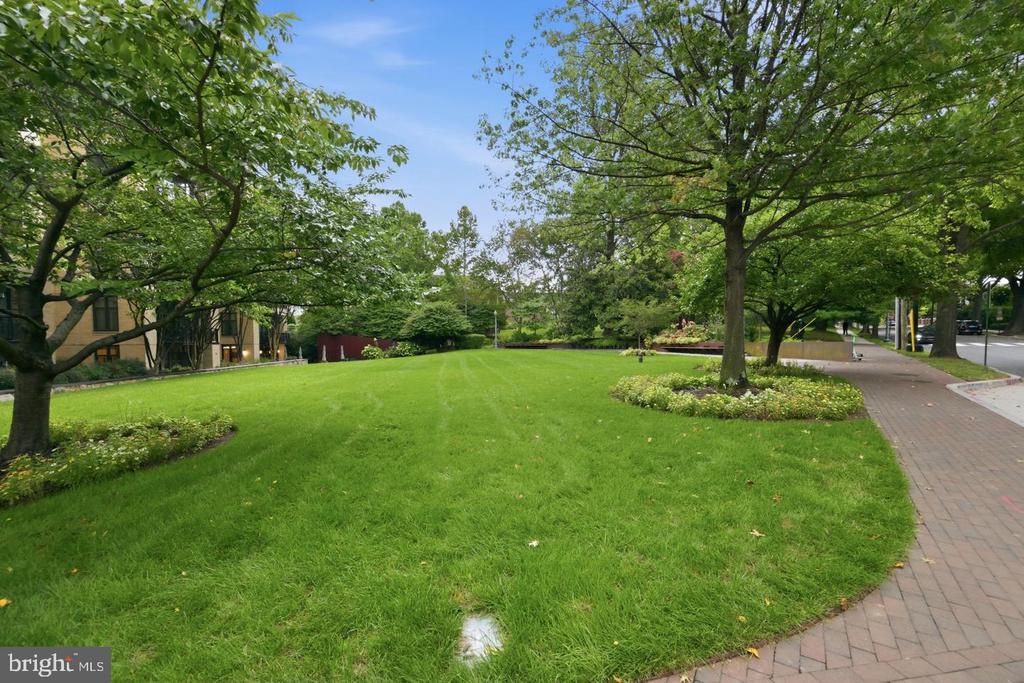 Landscaped lawn with mature trees and flower beds beside a brick sidewalk.
