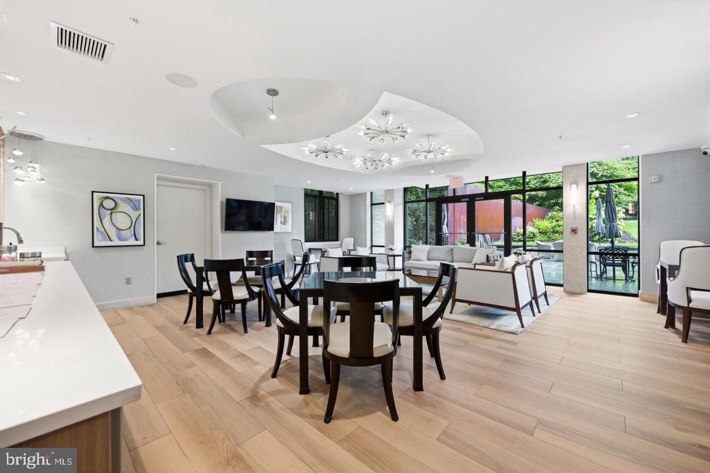 Furnished lounge and dining area with dark tables, sofas, and windows overlooking a pool.