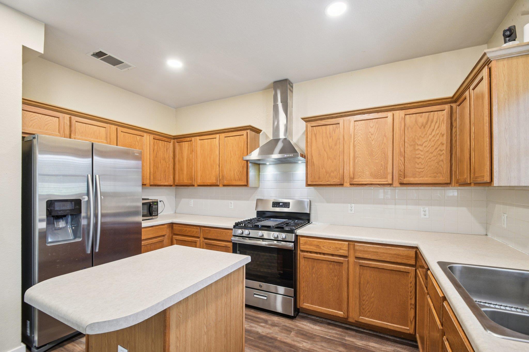 Kitchen with wood cabinets, a white-topped island, stainless appliances, and a gas range.