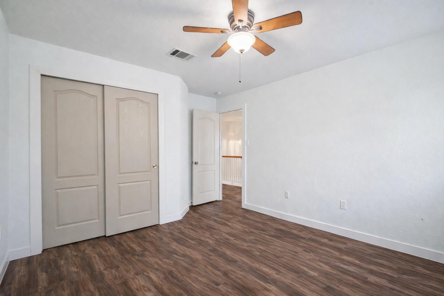 Empty bedroom with wood-look floors, closet doors, and a ceiling fan.