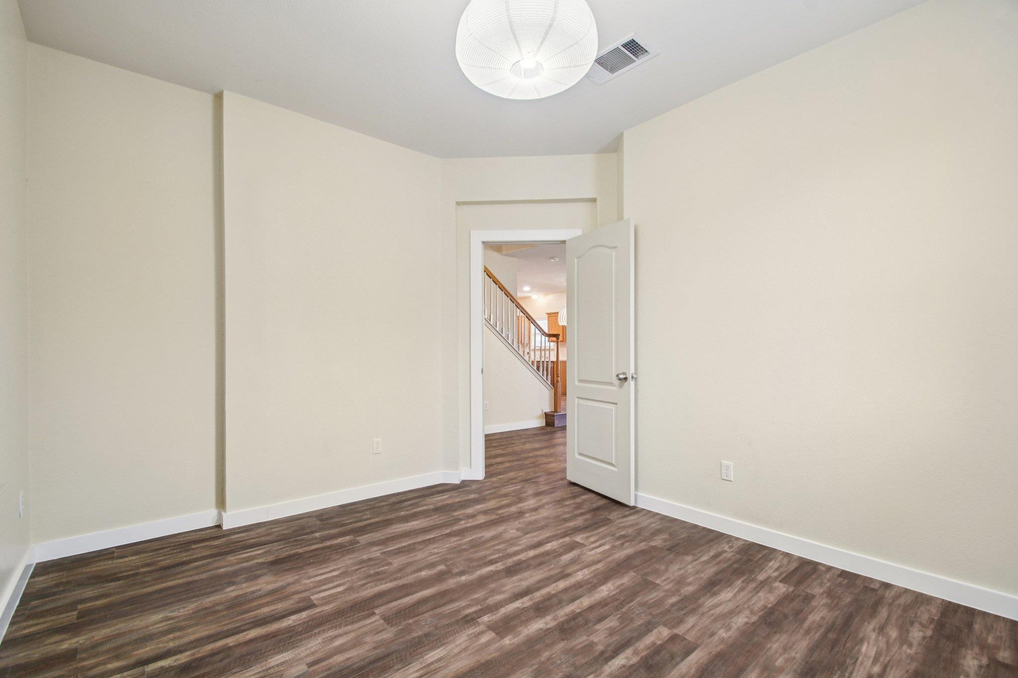Empty room with dark wood-look flooring and an open door to the staircase