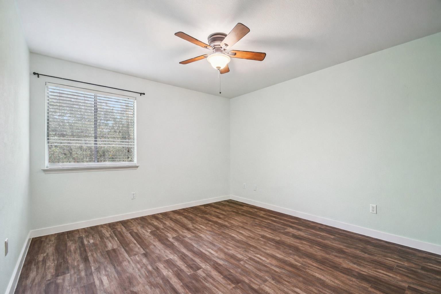 Empty bedroom with wood-look flooring, a window with blinds, and a ceiling fan.