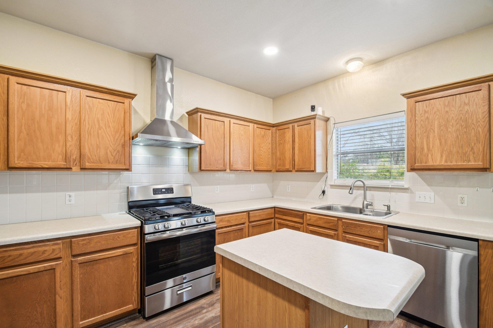 Kitchen with wood cabinets, stainless gas range, central island, and sink beneath a window.