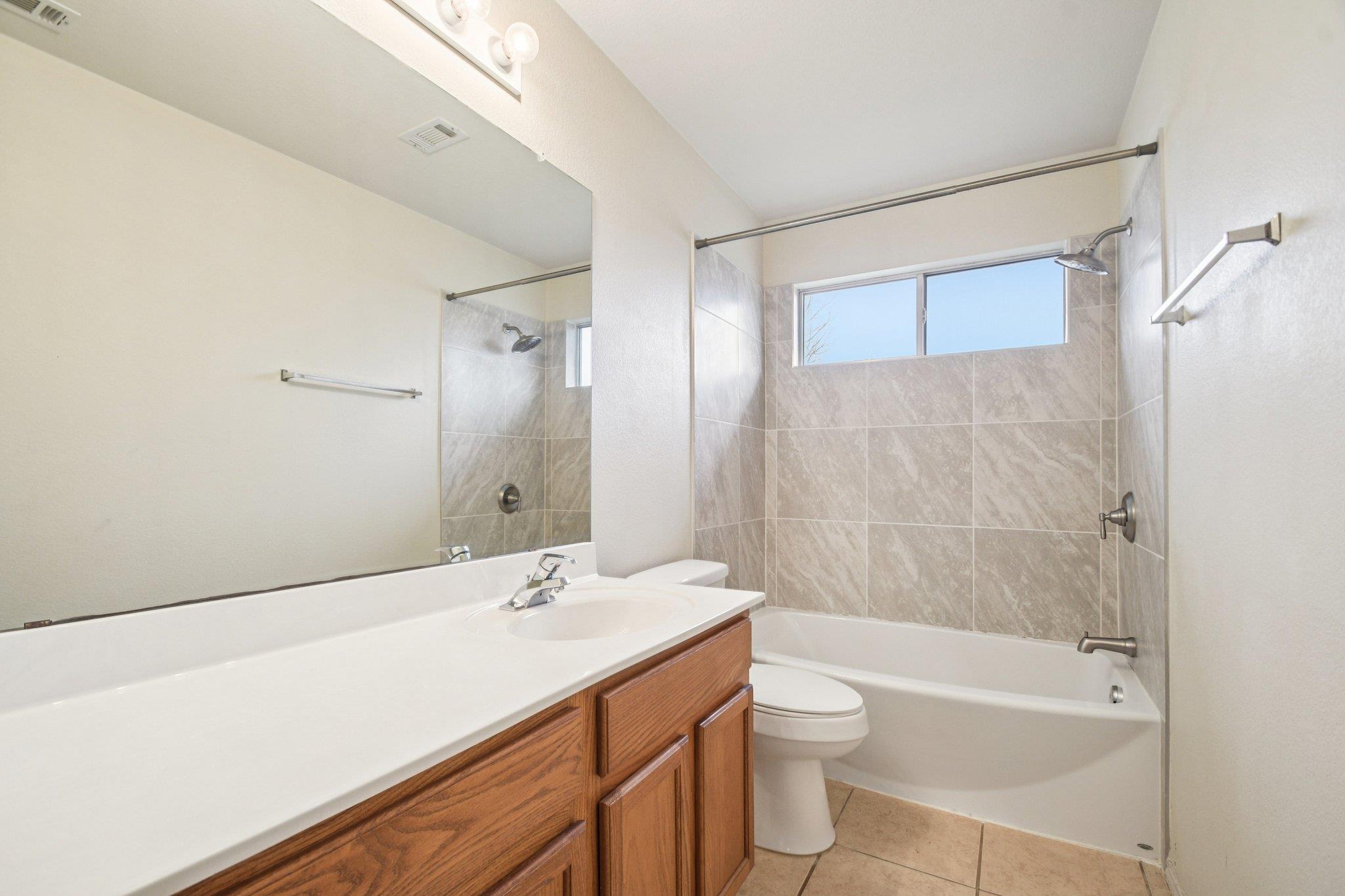 Bathroom with a wood vanity, large mirror, and tiled tub-shower beneath a wide window.