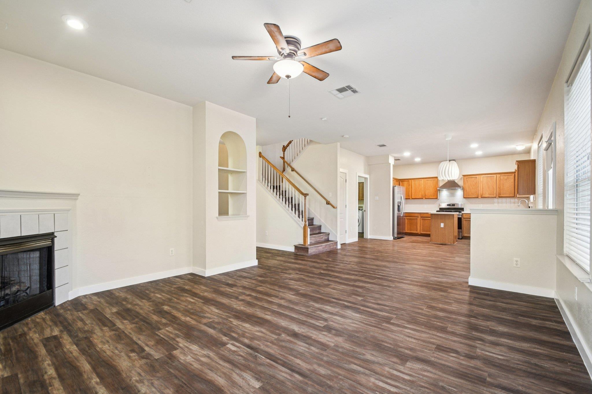 Open-plan living room and kitchen with a fireplace, staircase, and wood-look flooring.