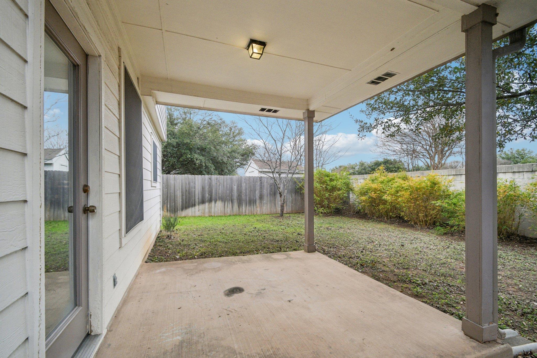 Covered back patio overlooking a fenced yard with shrubs and patchy grass.