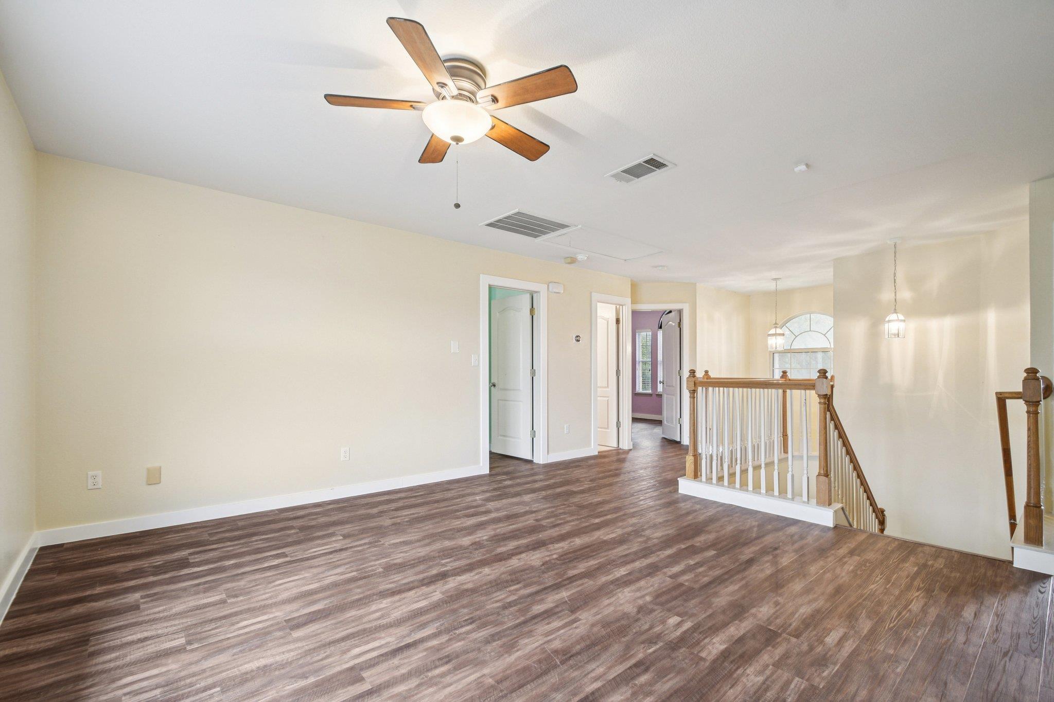 Empty upstairs landing with dark wood-look floors, a ceiling fan, and a wooden stair railing.