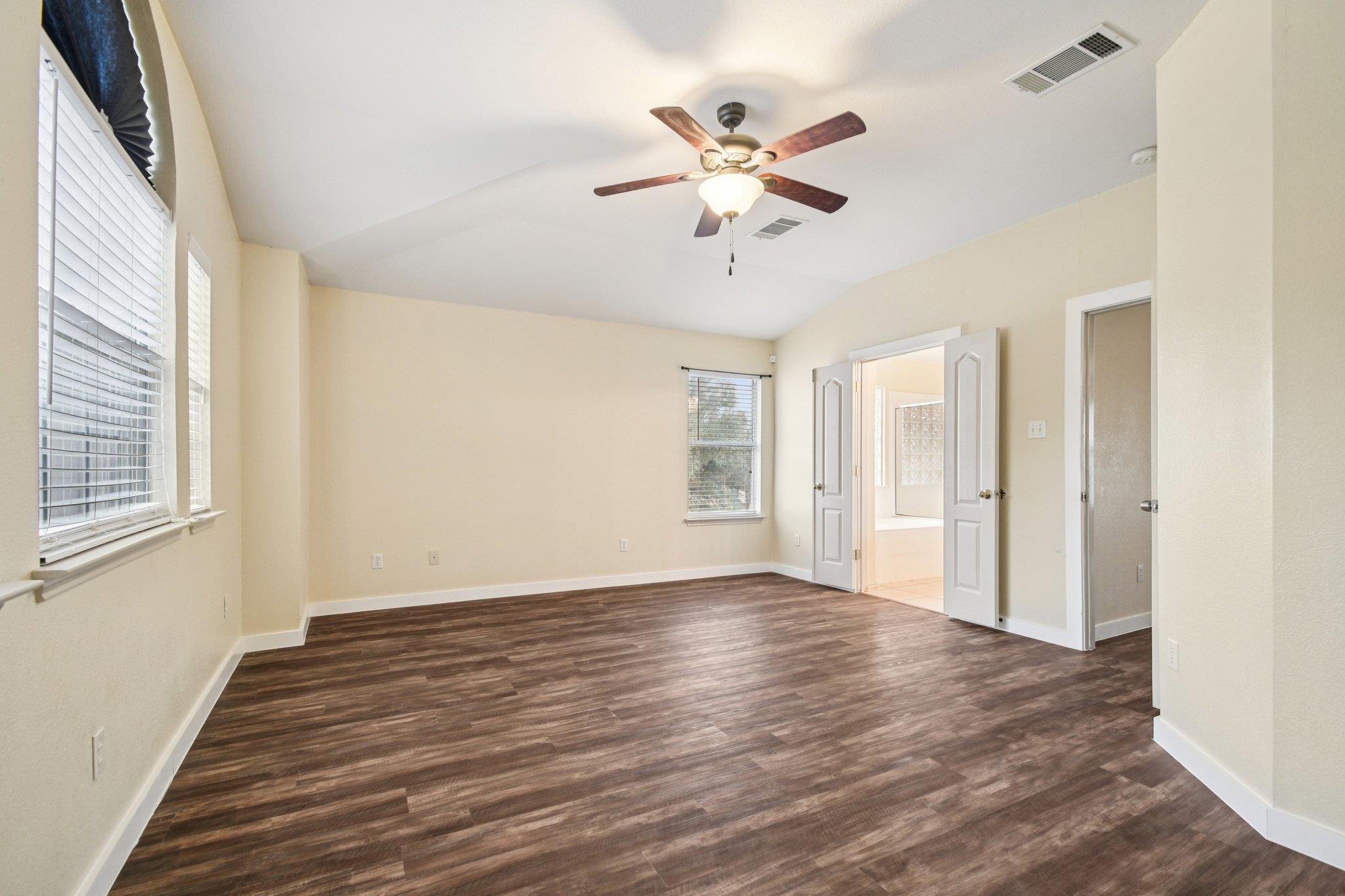 Empty bedroom with dark wood-look flooring, window blinds, and a lit ceiling fan.