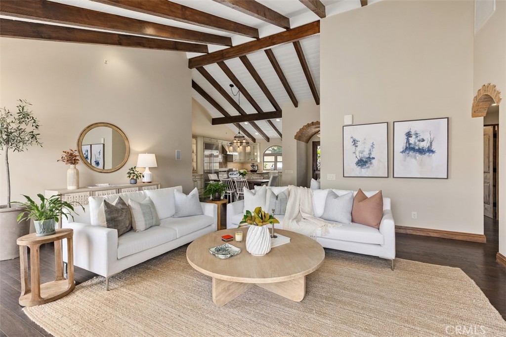 Living room with white sofas, a round wood coffee table, and exposed ceiling beams.