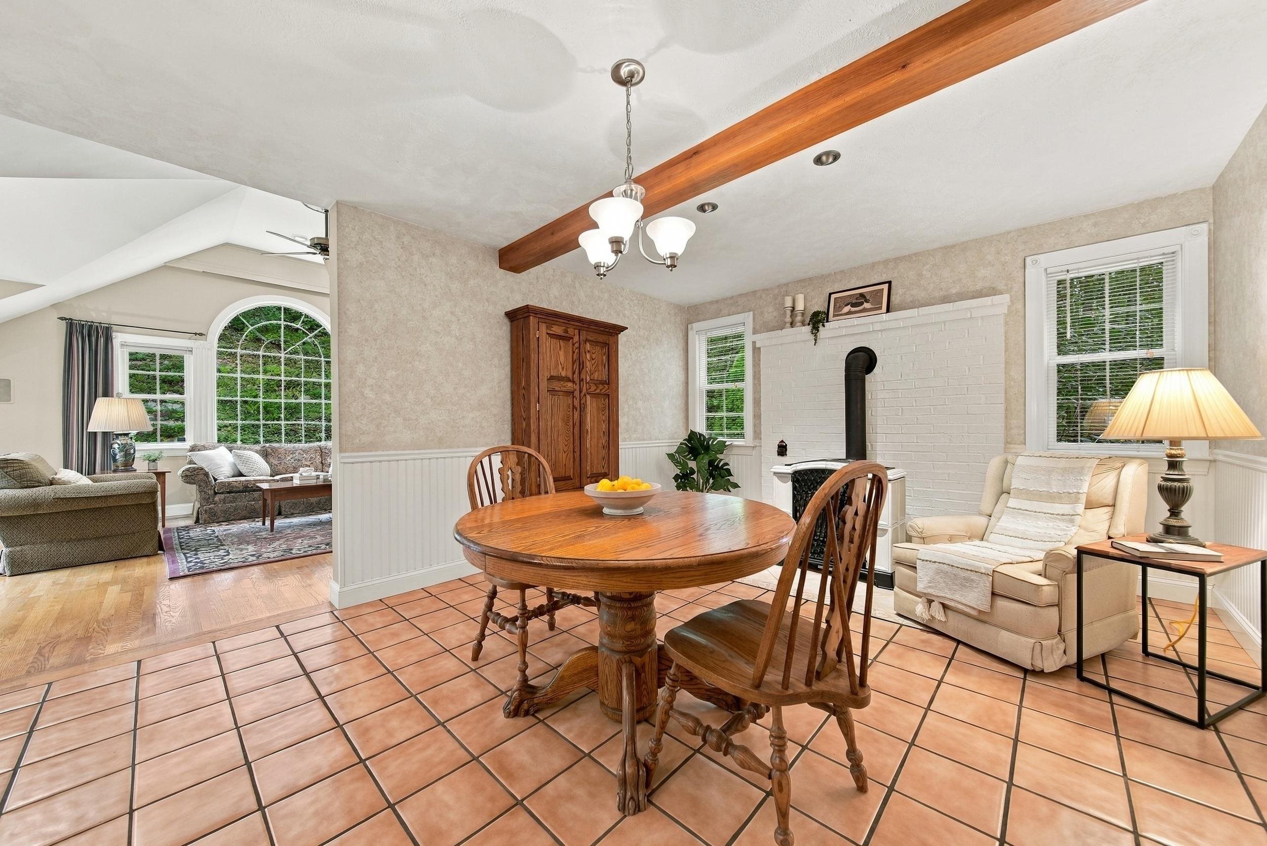 Dining room with a round wooden table, white brick fireplace, exposed beam, and arched window to the living room.