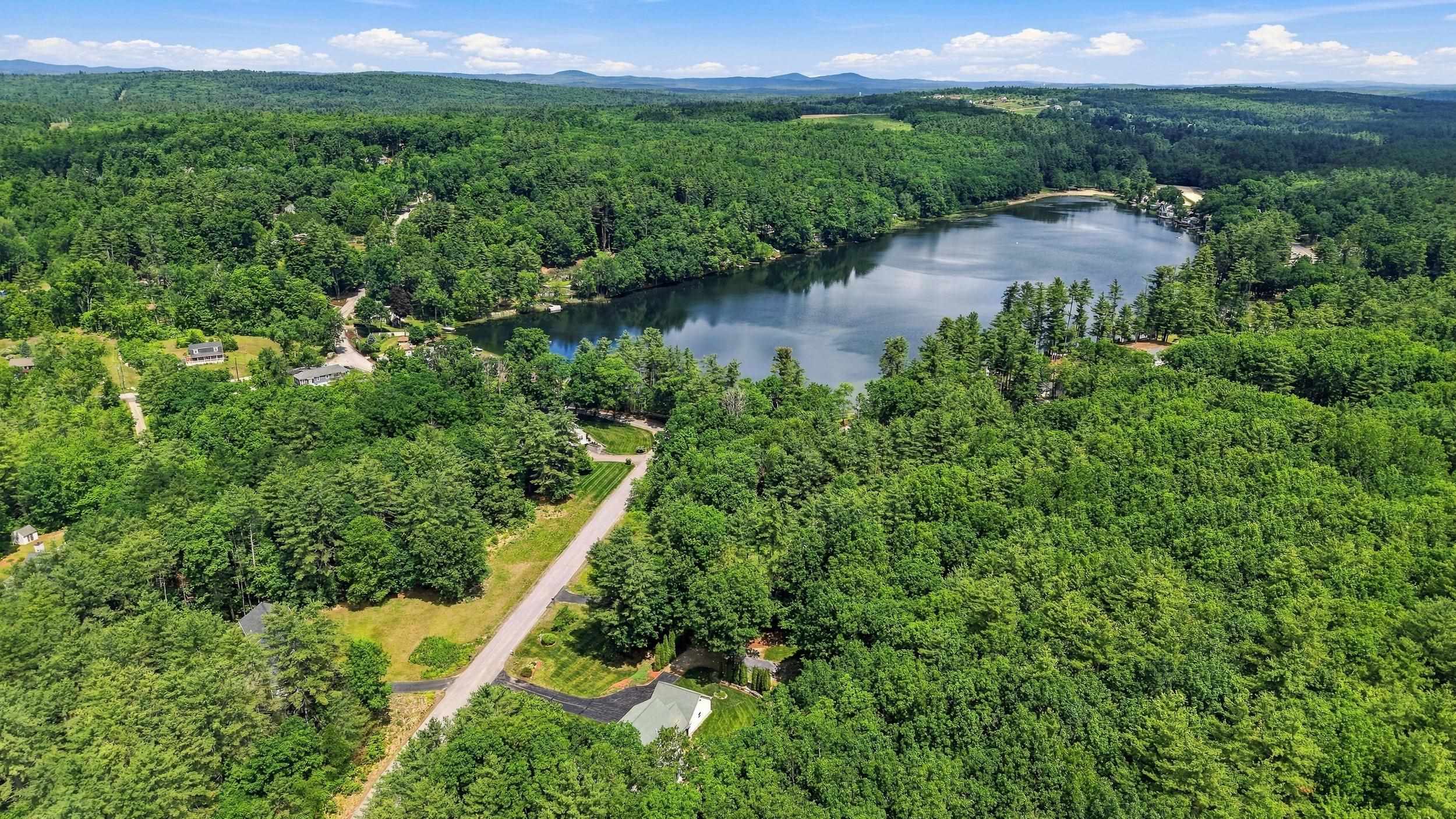 Aerial view of a wooded lake and surrounding homes, with a road leading toward the water.