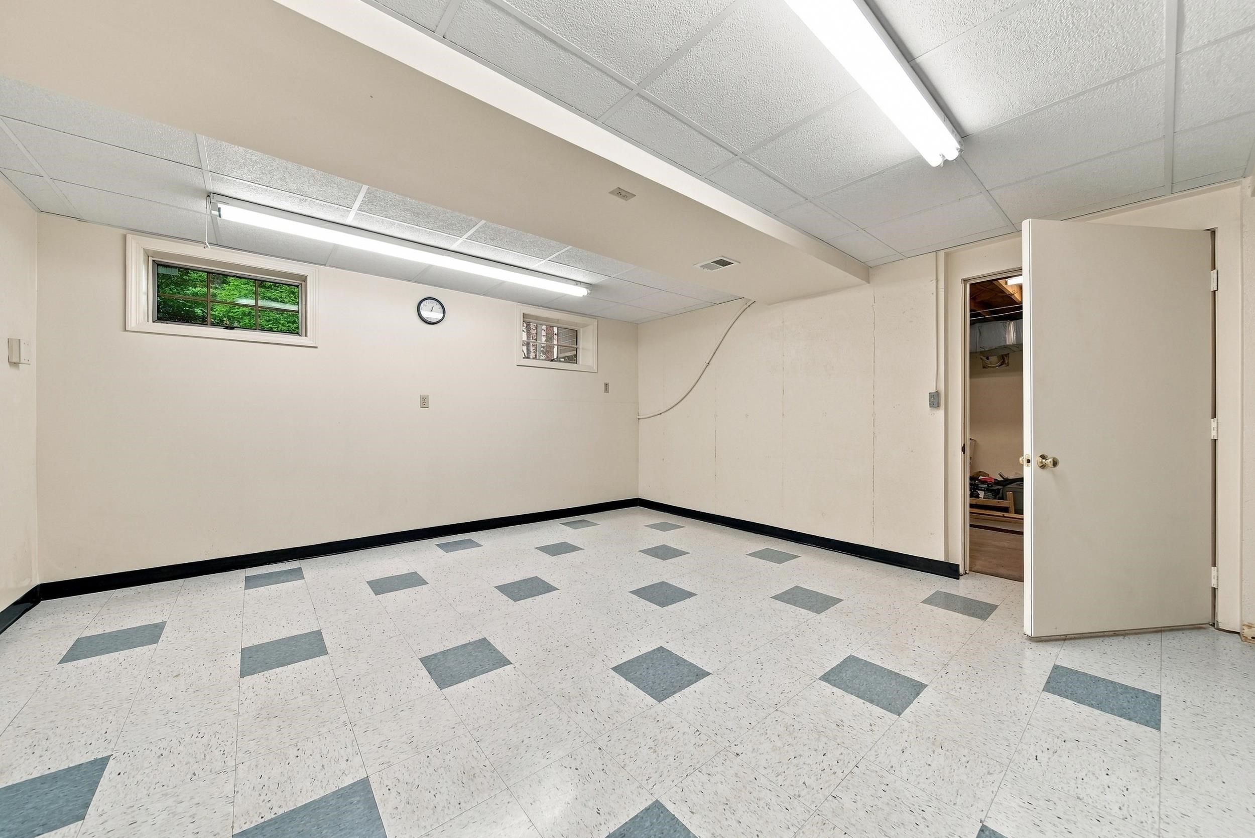 Empty room with a patterned tile floor, fluorescent lights, small windows, and an open door to storage.