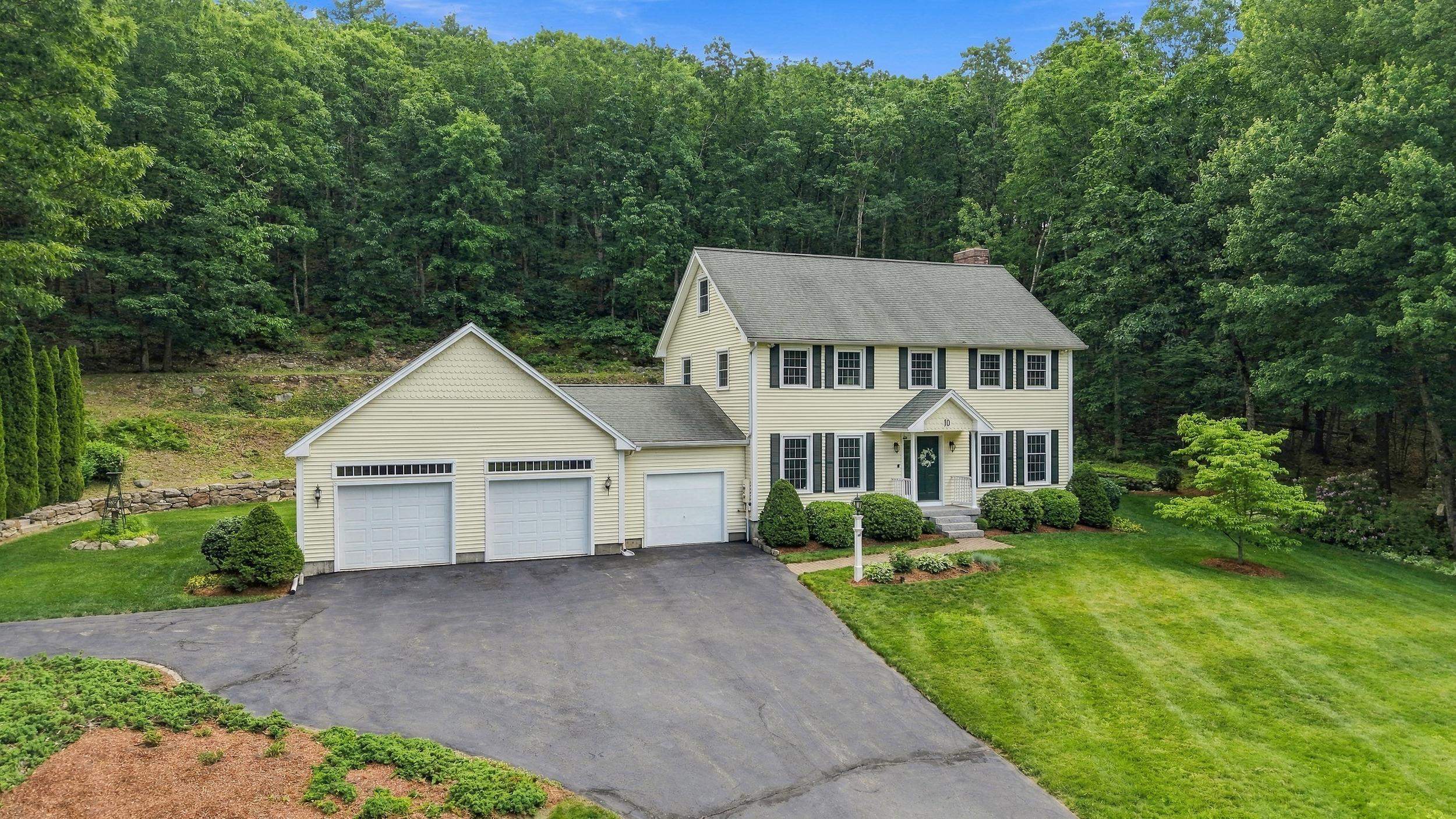 Pale yellow two-story home with a three-car garage, broad driveway, and wooded surroundings.