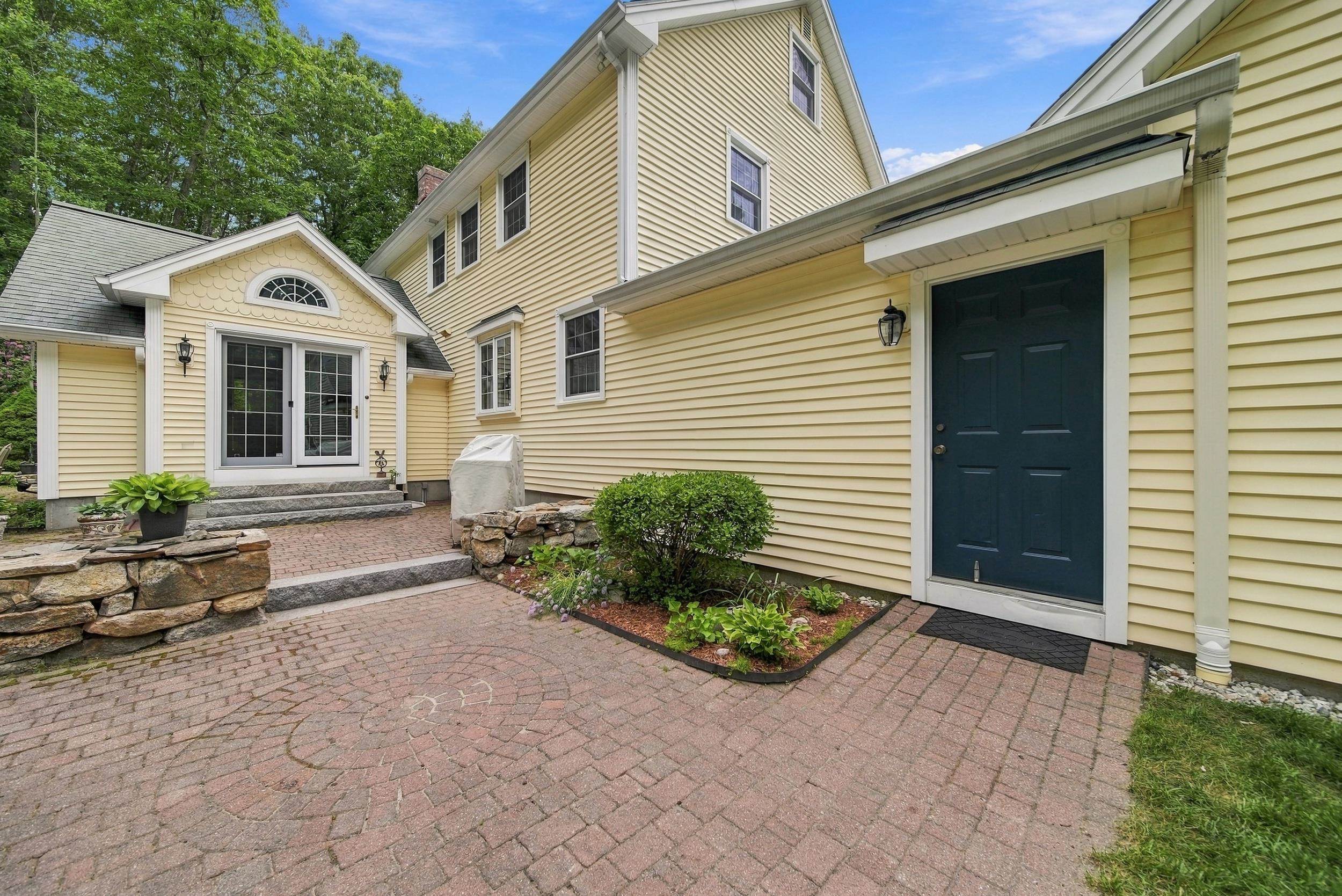 Yellow-sided home with dark blue doors, a brick patio, stone walls, and landscaped garden beds.