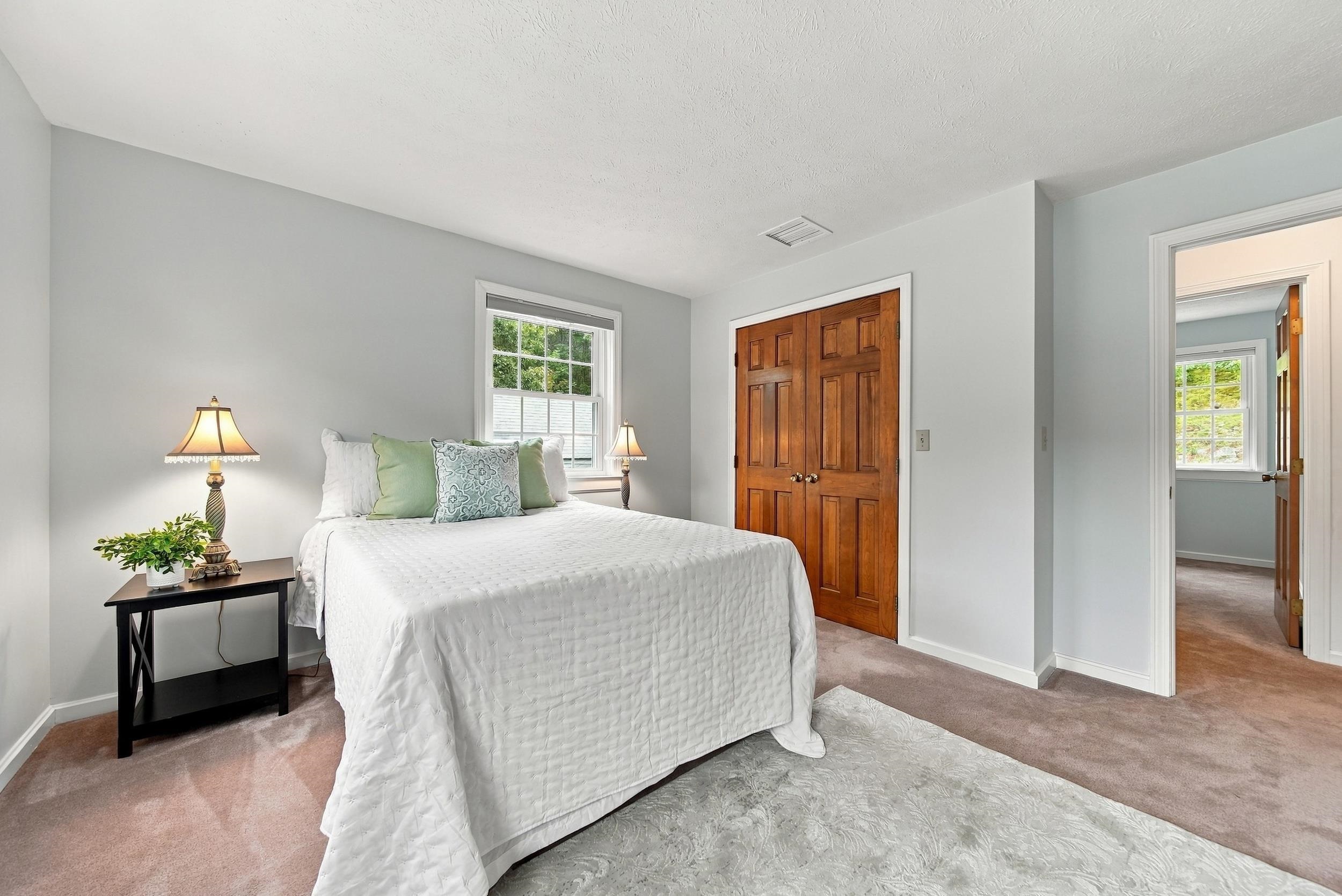 Staged bedroom with a white bed, pale green pillows, bedside lamps, and warm wood closet doors.