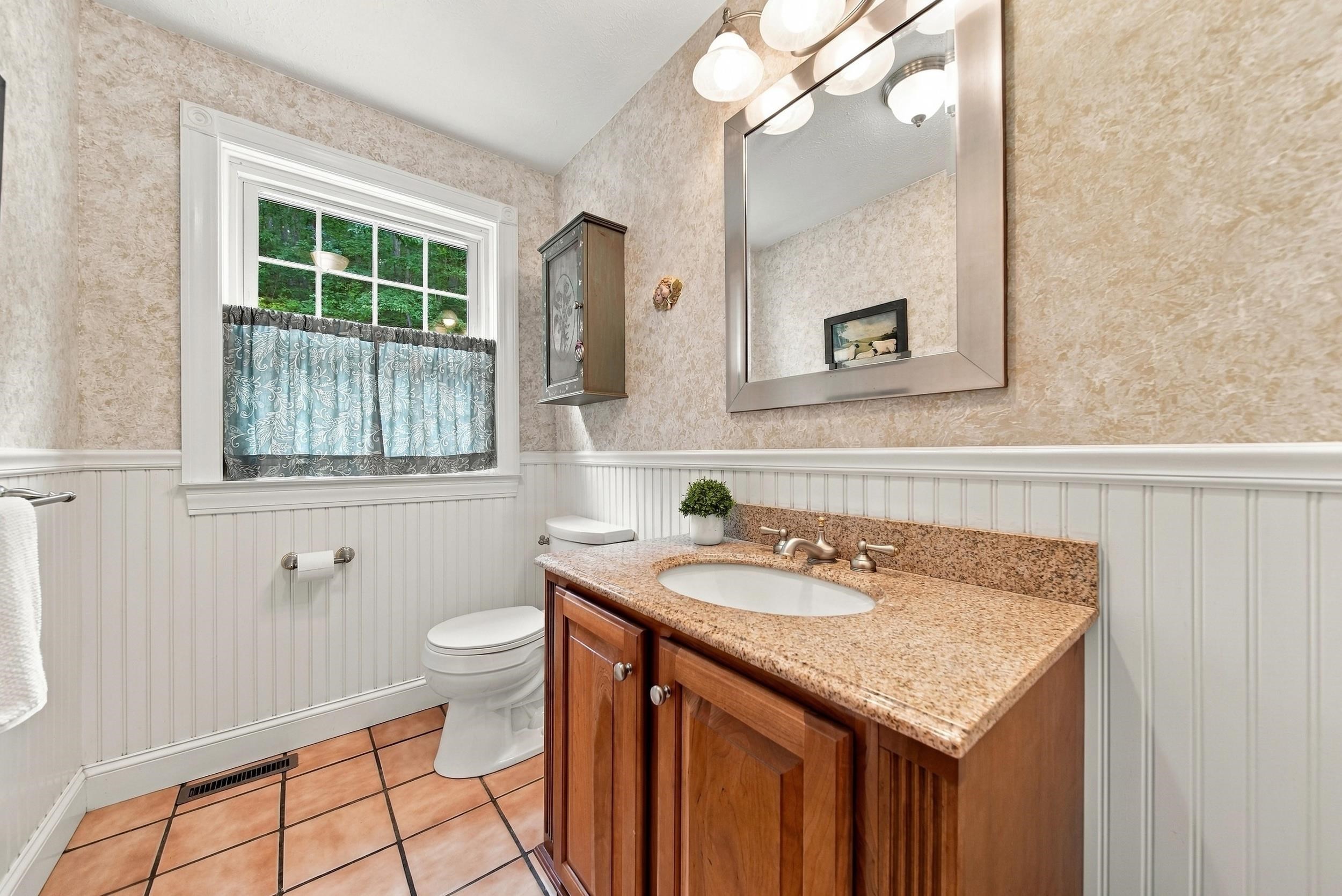 Bathroom with a wood vanity, speckled countertop, white beadboard wainscoting, and curtained window.