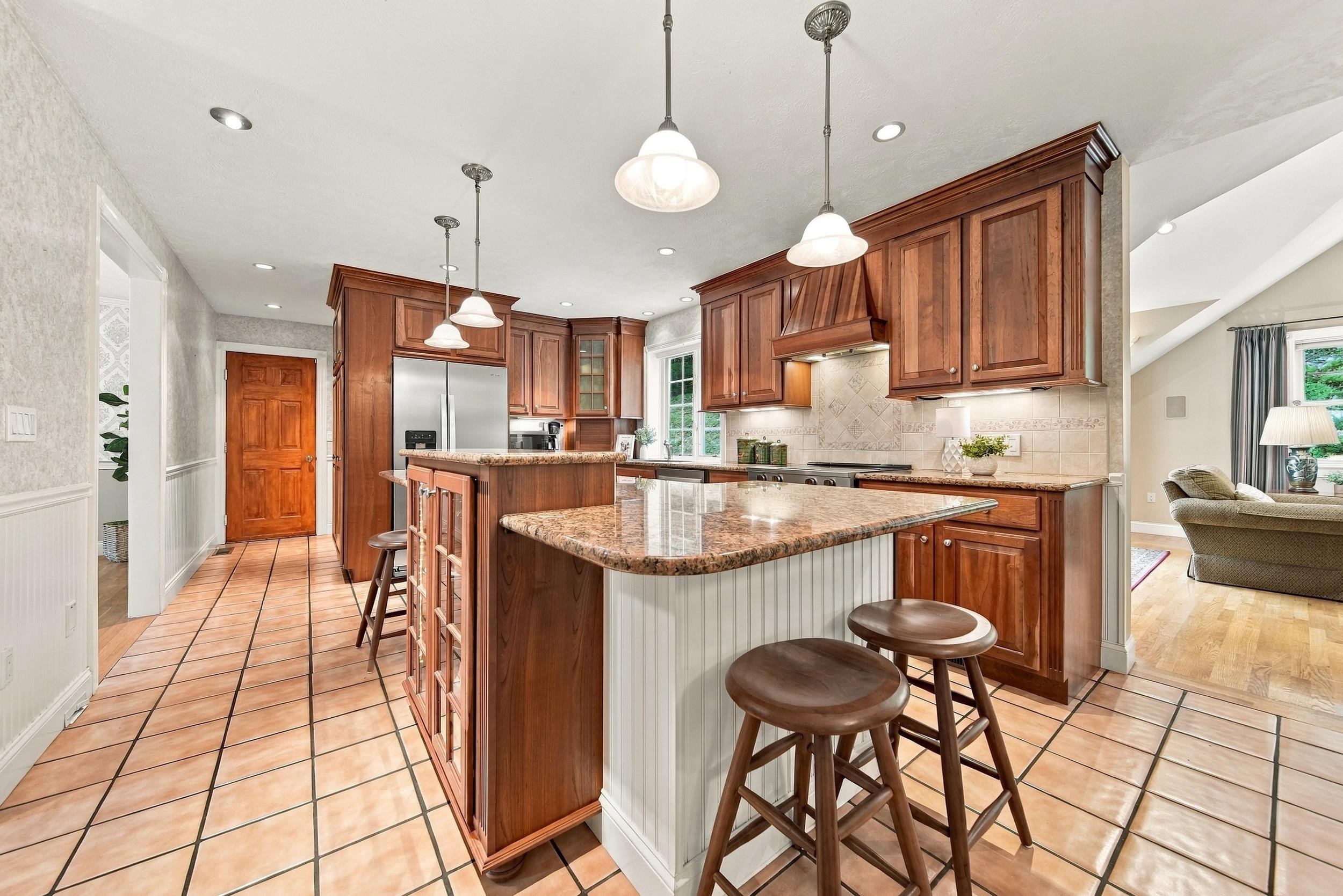 Kitchen with rich wood cabinets, granite island, tiled floors, and pendant lights.