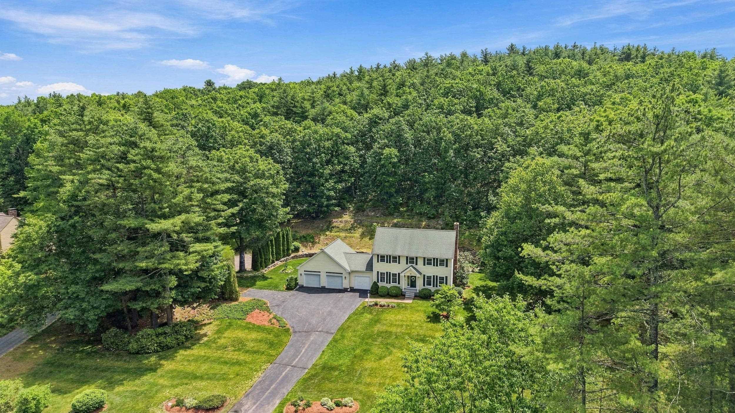 Aerial view of a two-story house with a three-car garage and wooded surroundings.