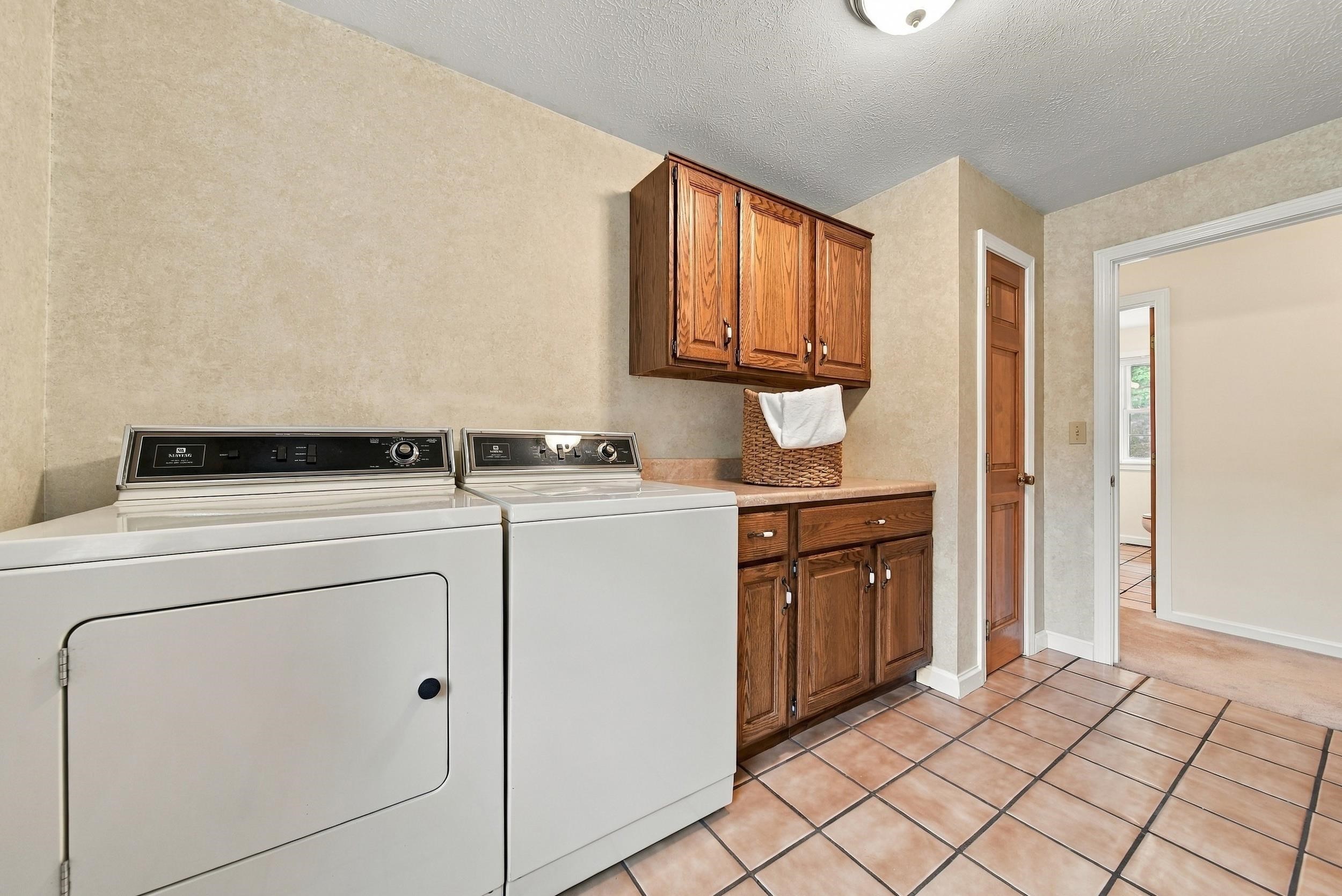 Laundry room with white washer and dryer, wood cabinetry, and terracotta-colored tile floor.