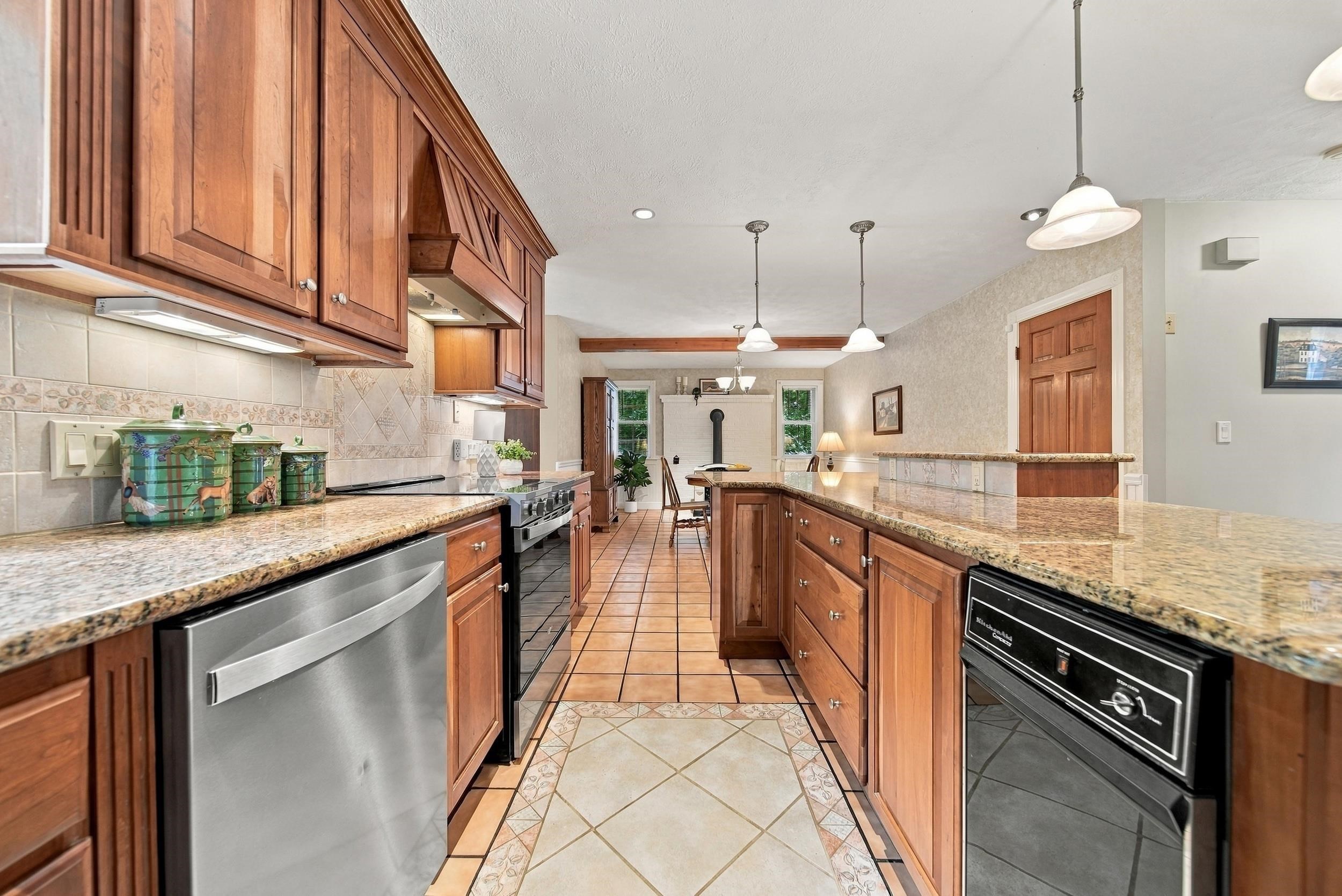 Kitchen with warm wood cabinetry, granite counters, stainless appliances, and a tiled floor.