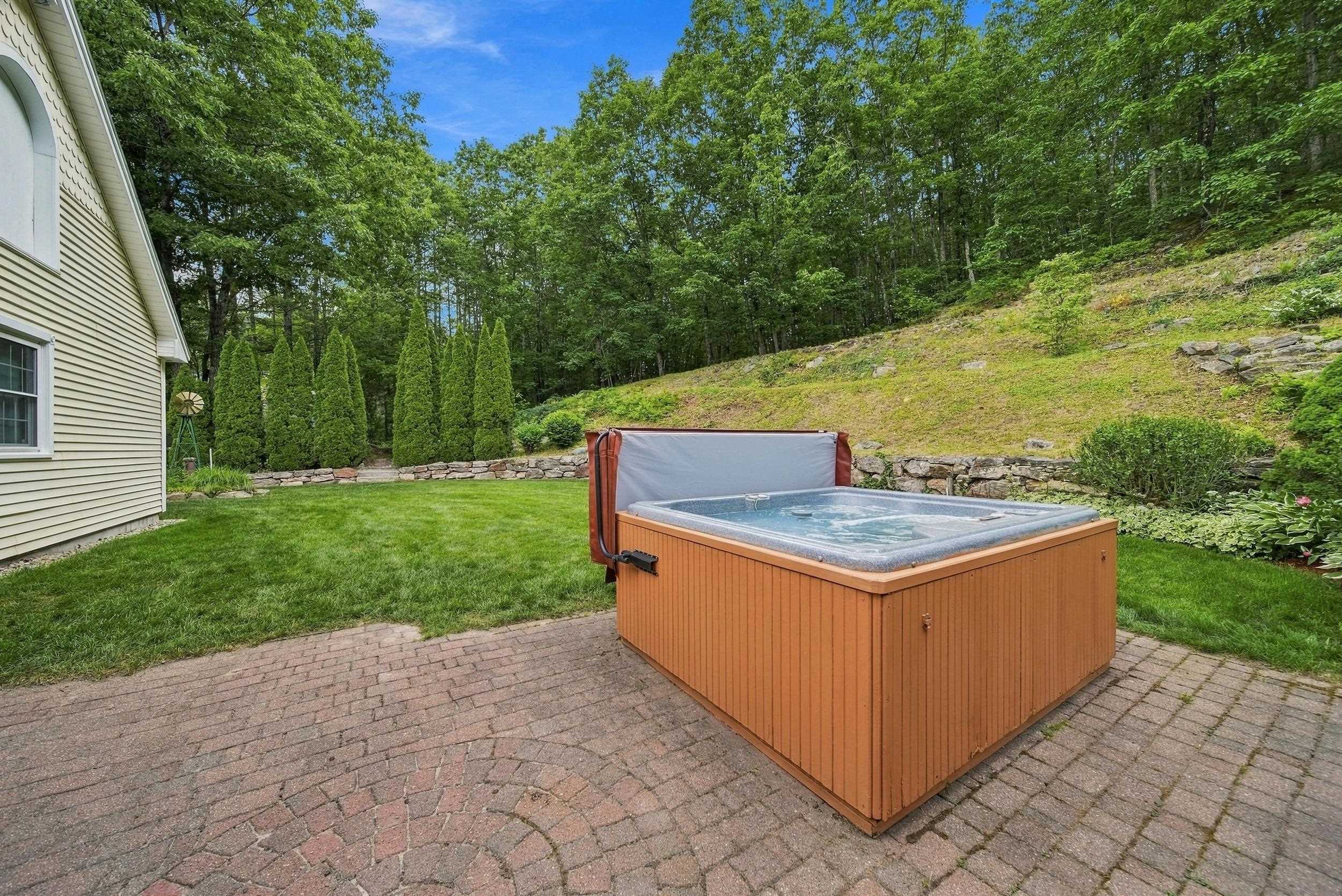 Backyard hot tub on a brick patio beside a lawn and wooded hillside.