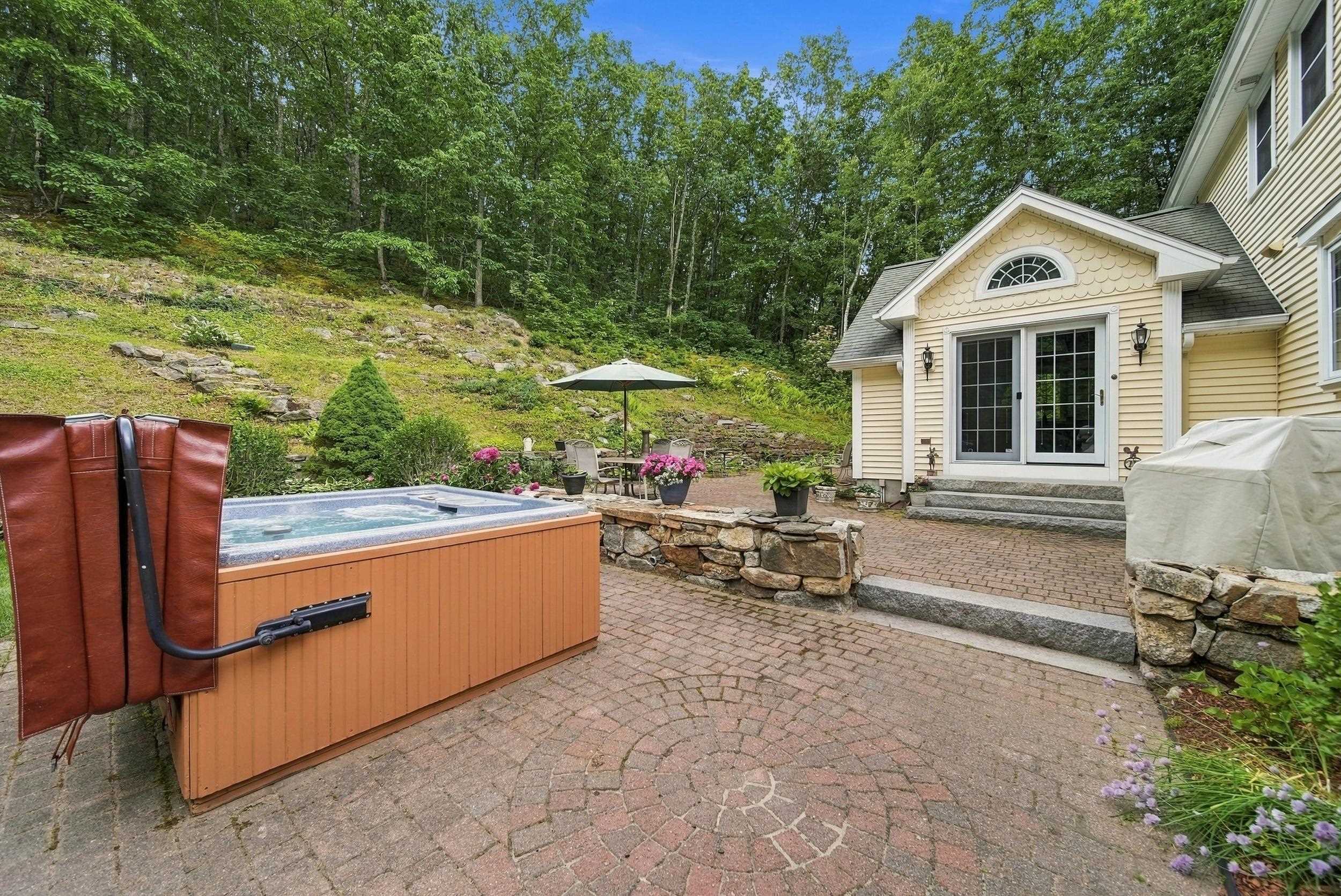 Back patio with a hot tub, brick paving, stone wall, and wooded hillside.