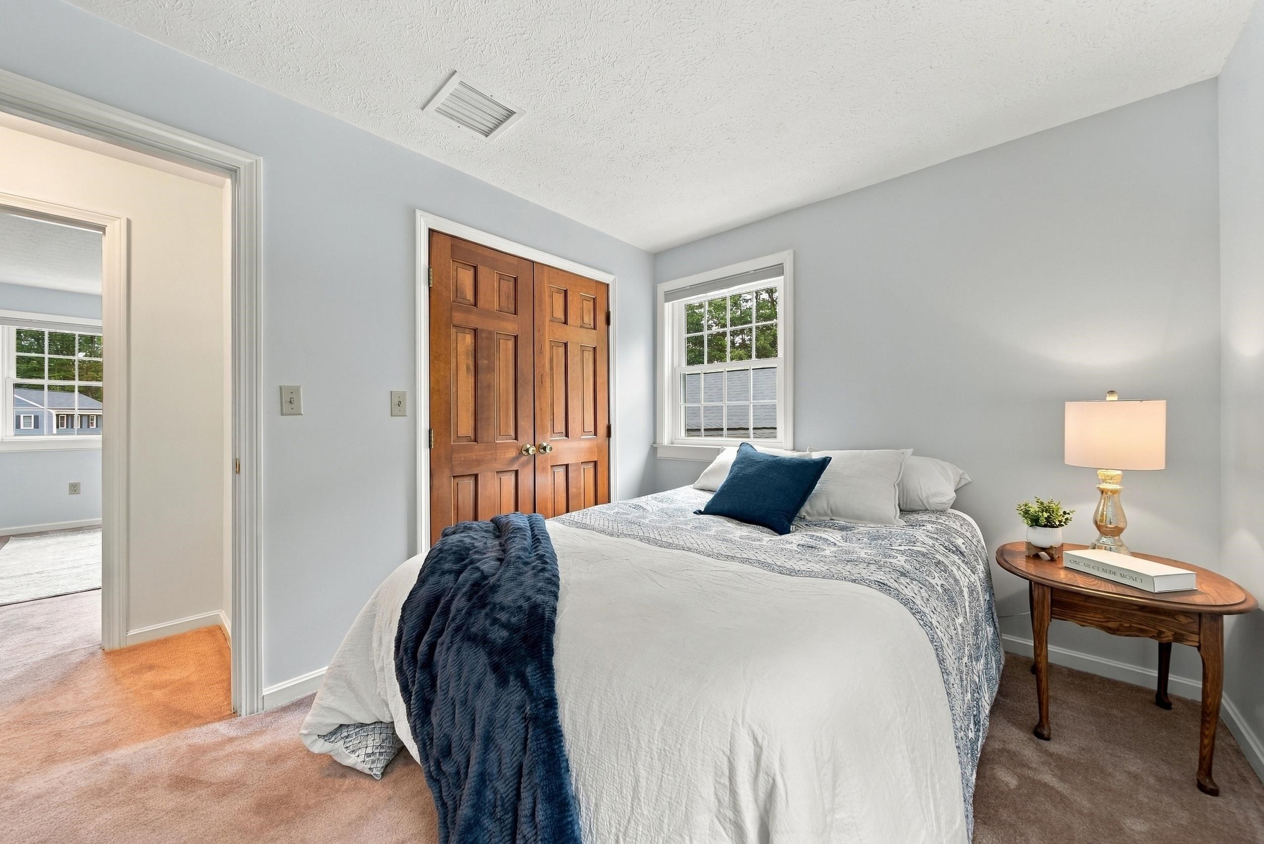 Bedroom with a white bed, navy accents, wooden double closet doors, and a bedside table with a lamp.
