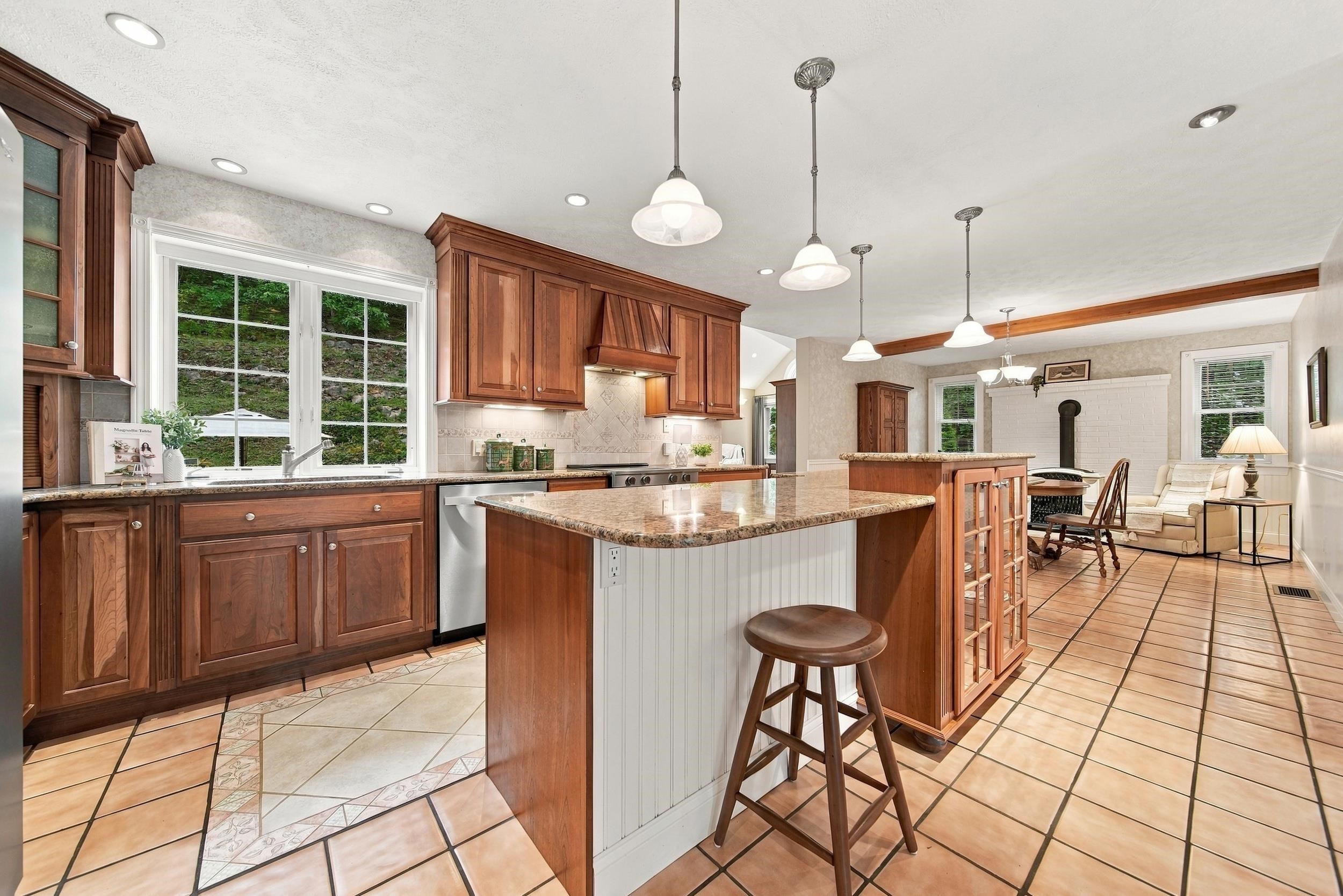 Kitchen with rich wood cabinets and a large granite island opening to a sitting area.