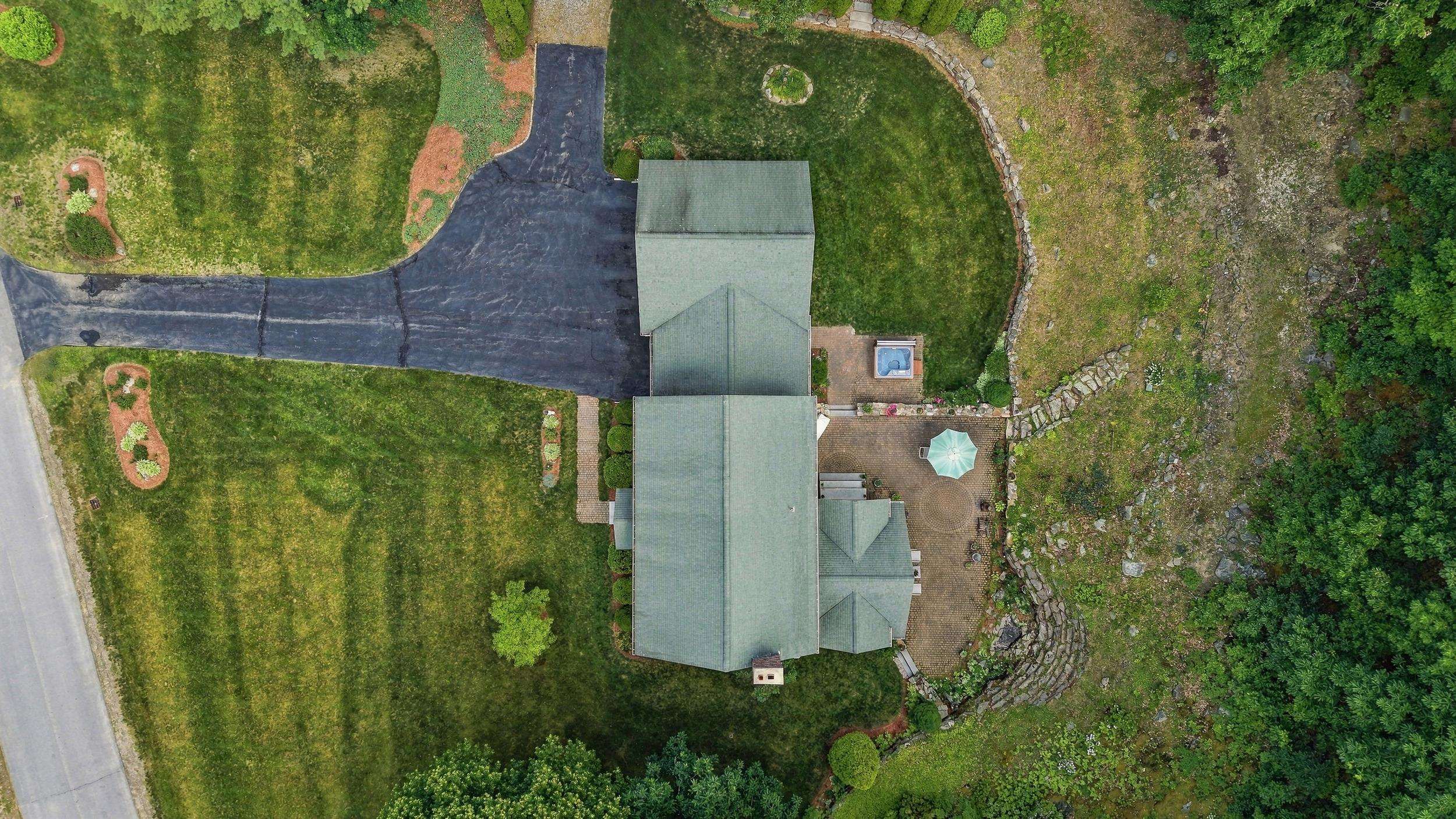 Aerial view of a landscaped house with a long driveway, stone walls, and a small pool.