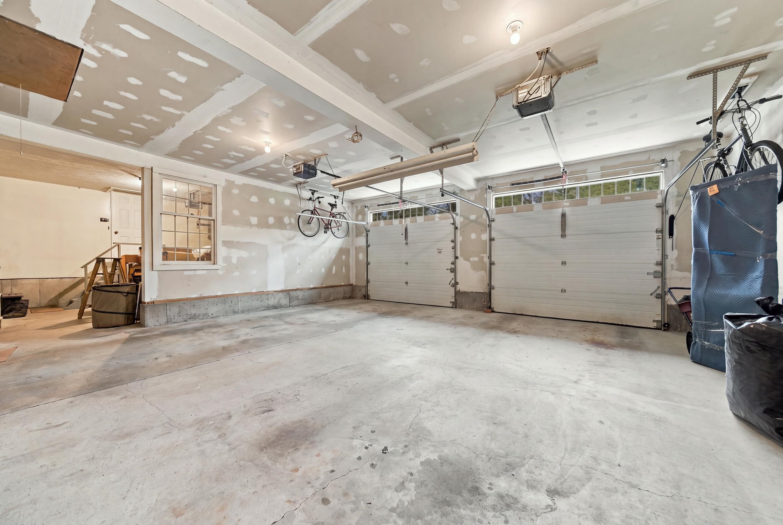 Two-car garage with unfinished drywall, concrete floor, and bicycles hanging overhead.