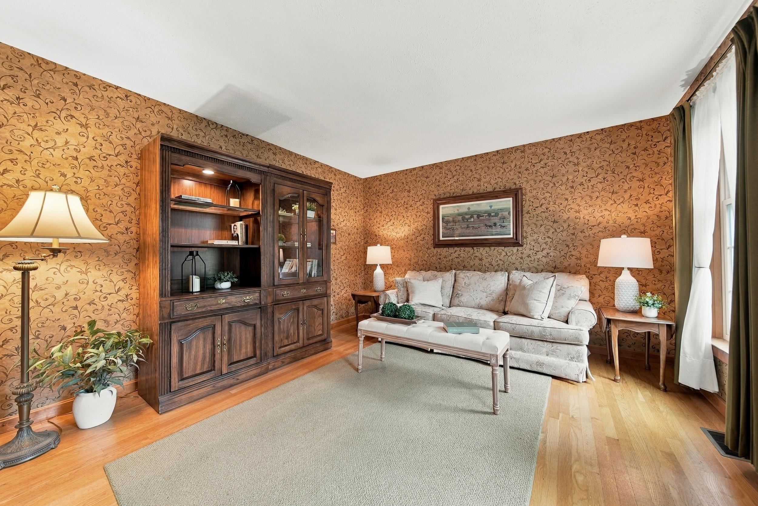 Furnished living room with ornate patterned wallpaper, built-in wooden shelving, and a pale sofa.