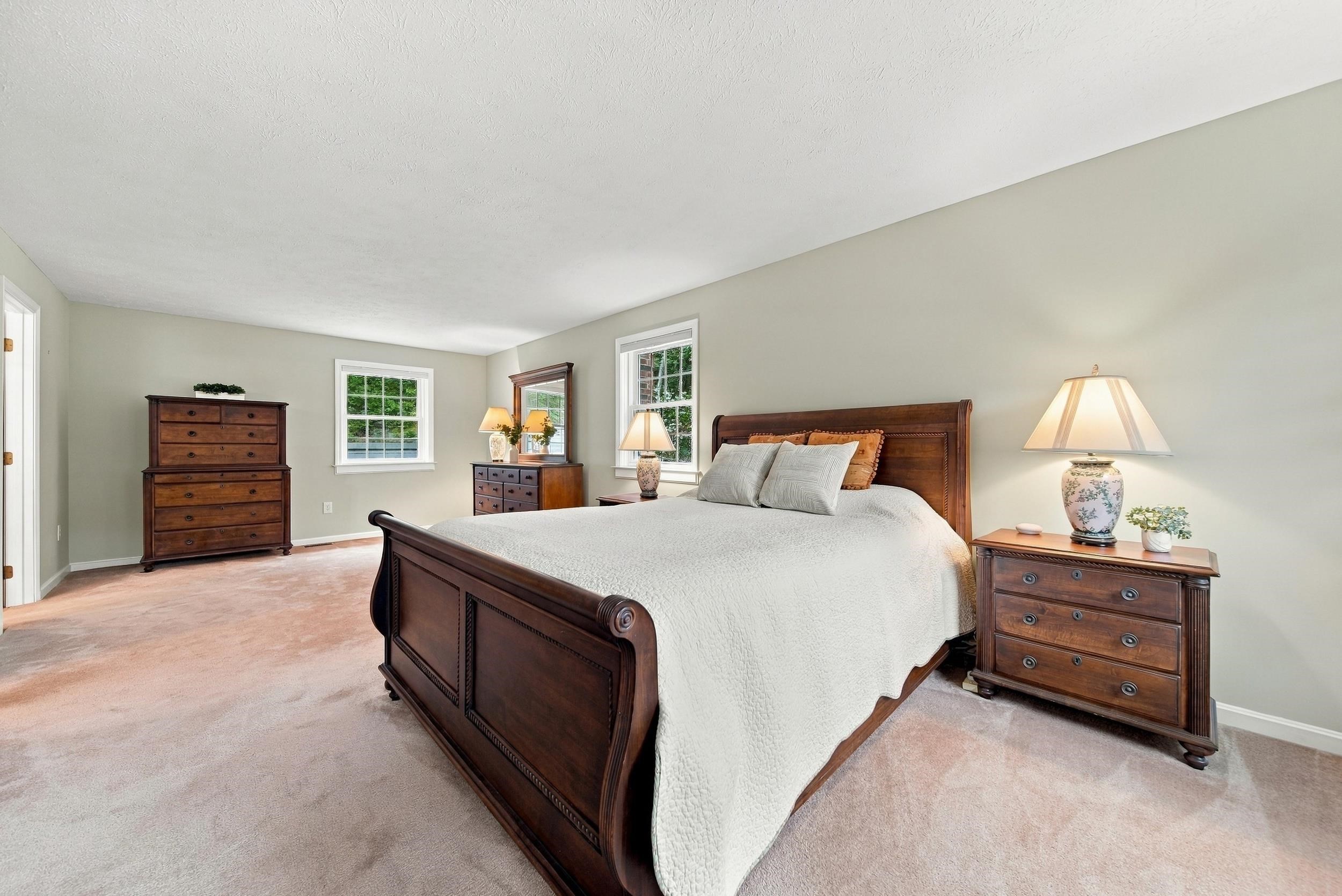 Furnished bedroom with a dark wood bed, matching dressers, and two windows.