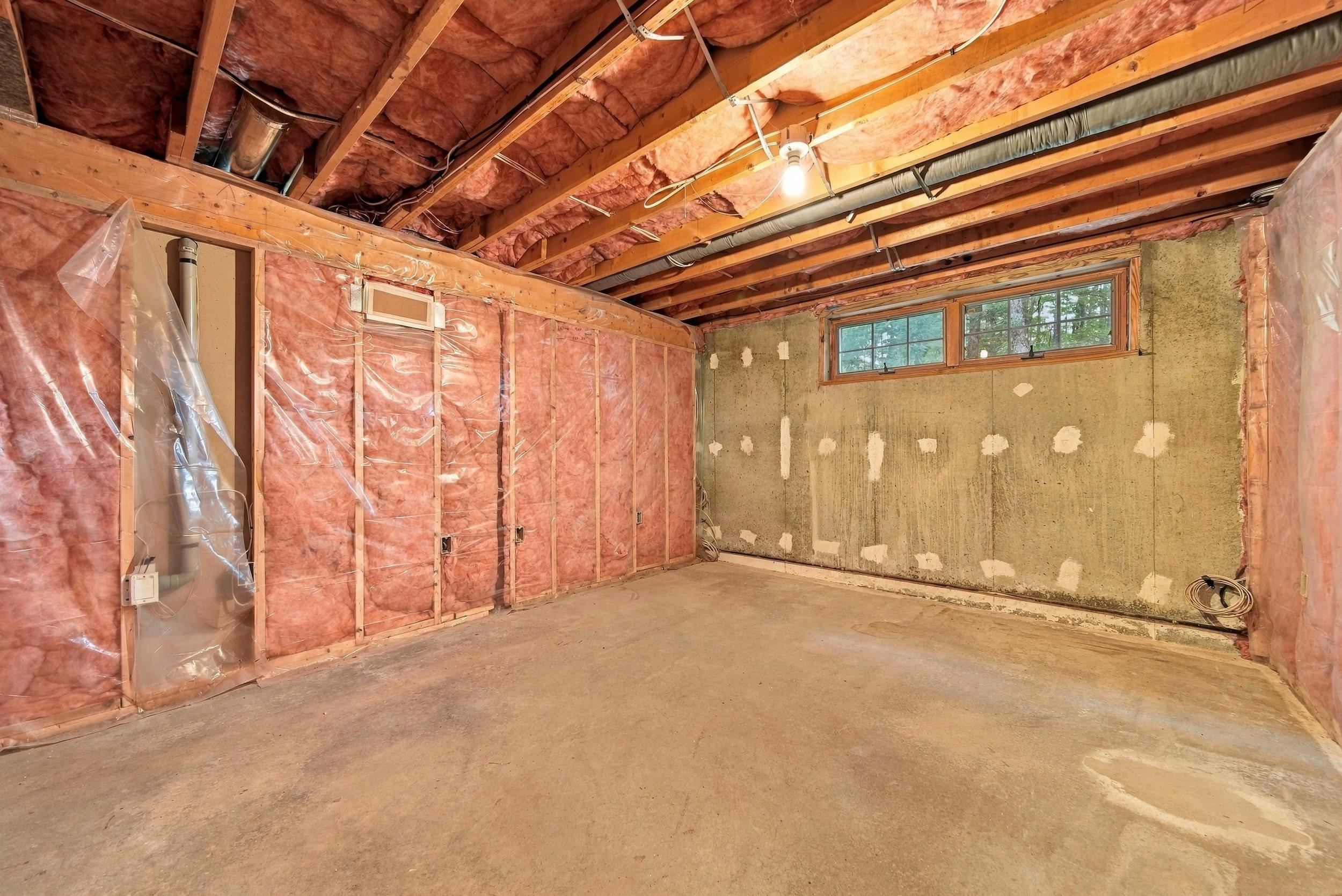 Unfinished basement with exposed insulation, ceiling joists, concrete floor, and two high-set windows.