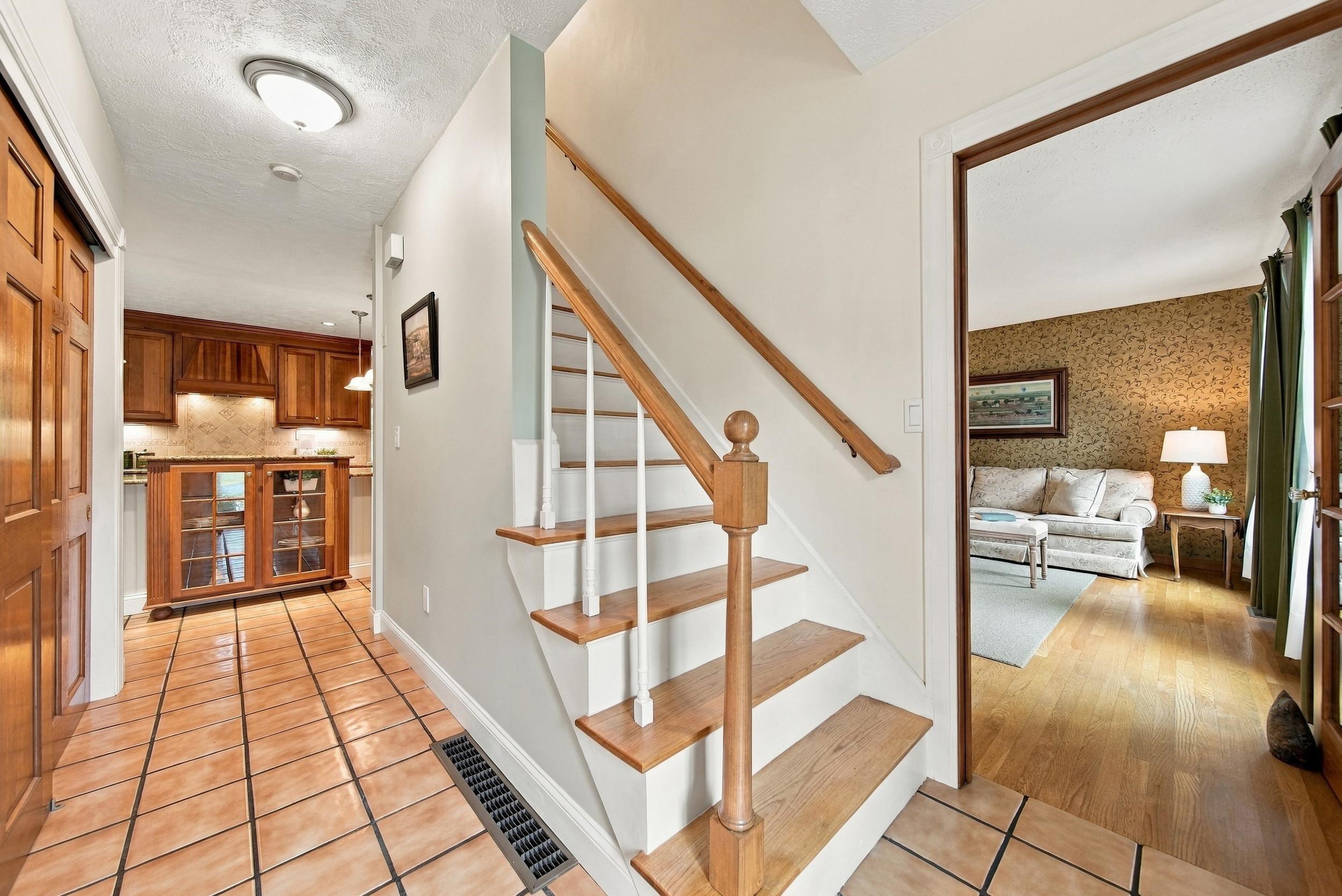Foyer with a wood-trimmed staircase, tiled floor, kitchen, and living room.