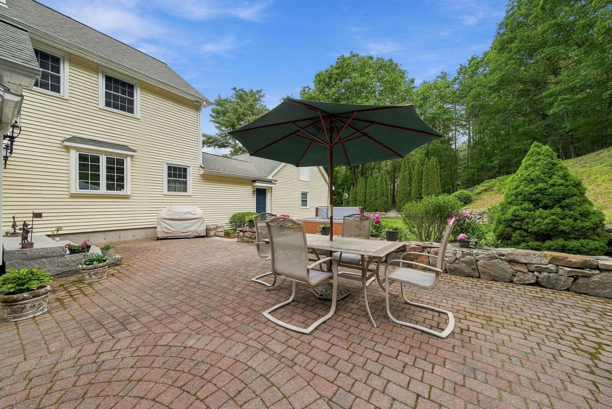 Brick patio with umbrella-shaded dining set, hot tub, and stone wall beside the home.