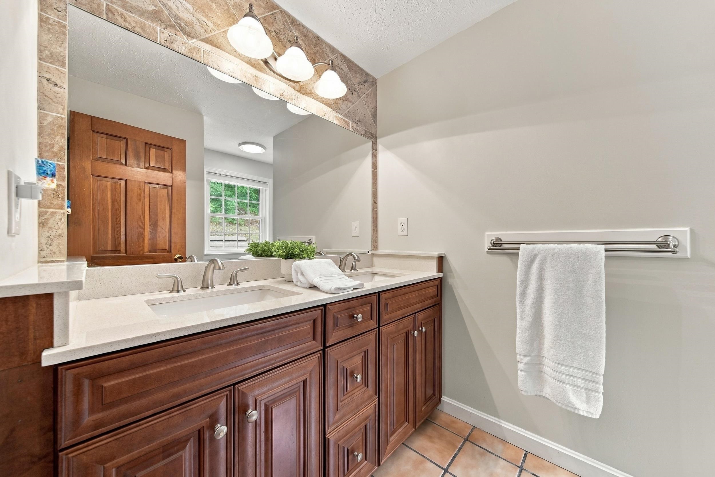 Bathroom with a double-sink vanity, dark wood cabinets, and a large stone-framed mirror.