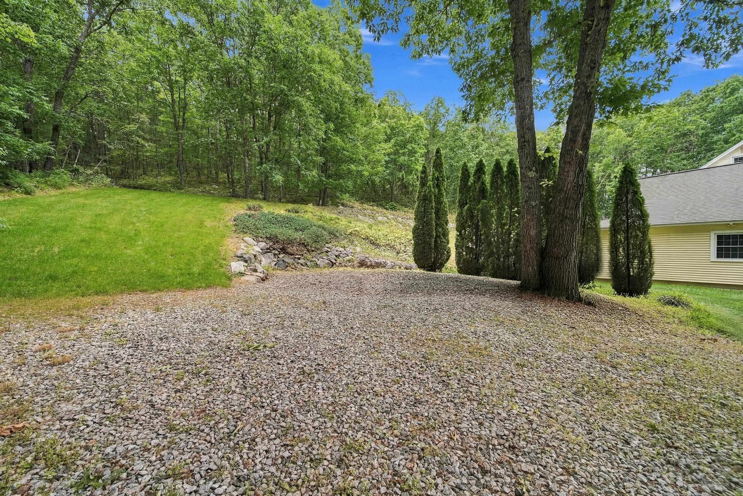 Gravel yard beside a house, with a lawn, mature trees, and a rock-edged planting bed.