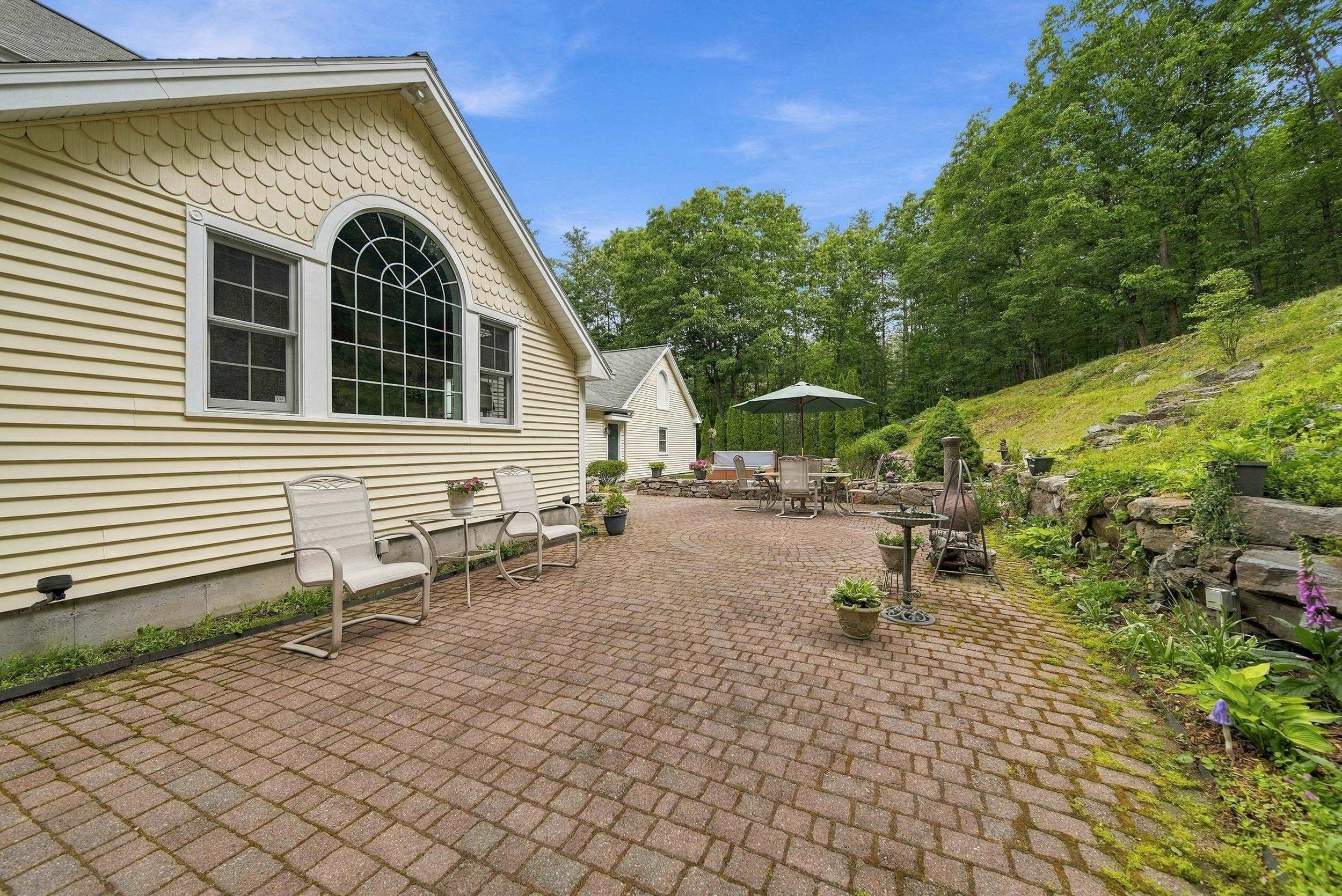 Brick patio beside a cream-sided home, with outdoor seating, an umbrella, and a landscaped stone hillside.