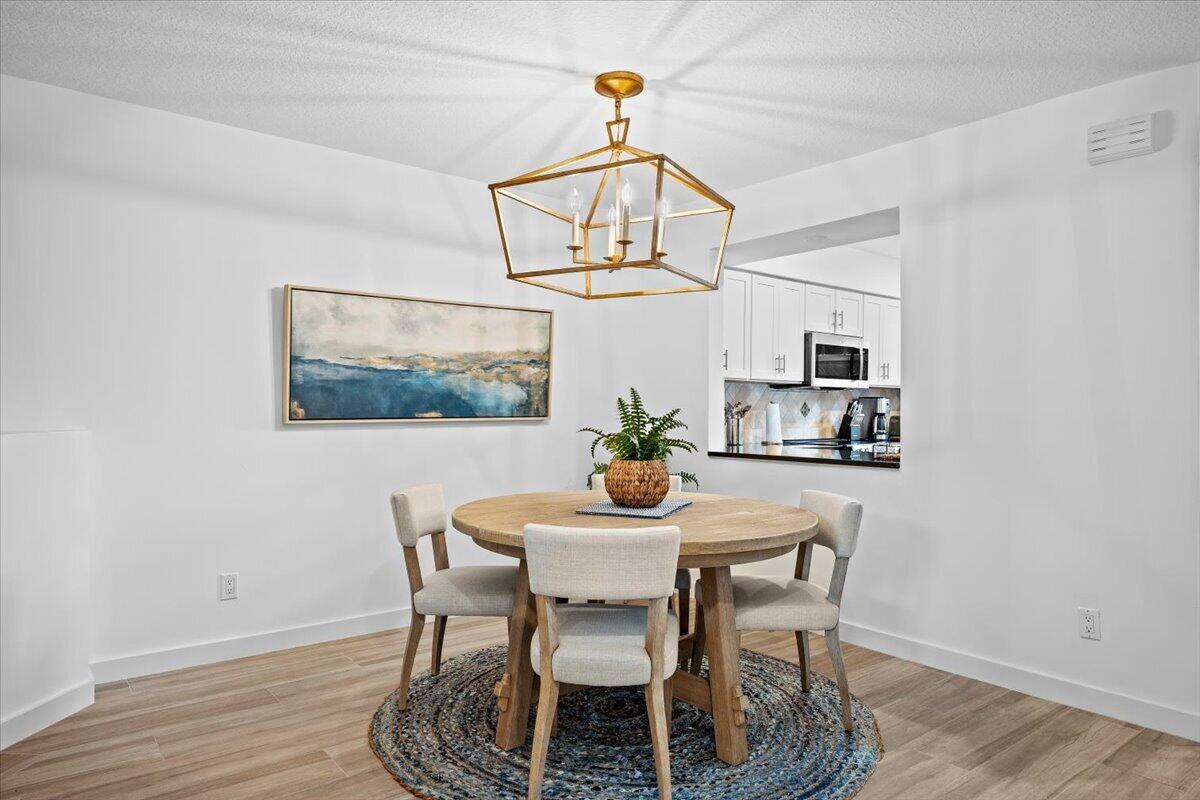 Dining room with a round wood table, woven rug, and gold geometric chandelier beside a white kitchen.