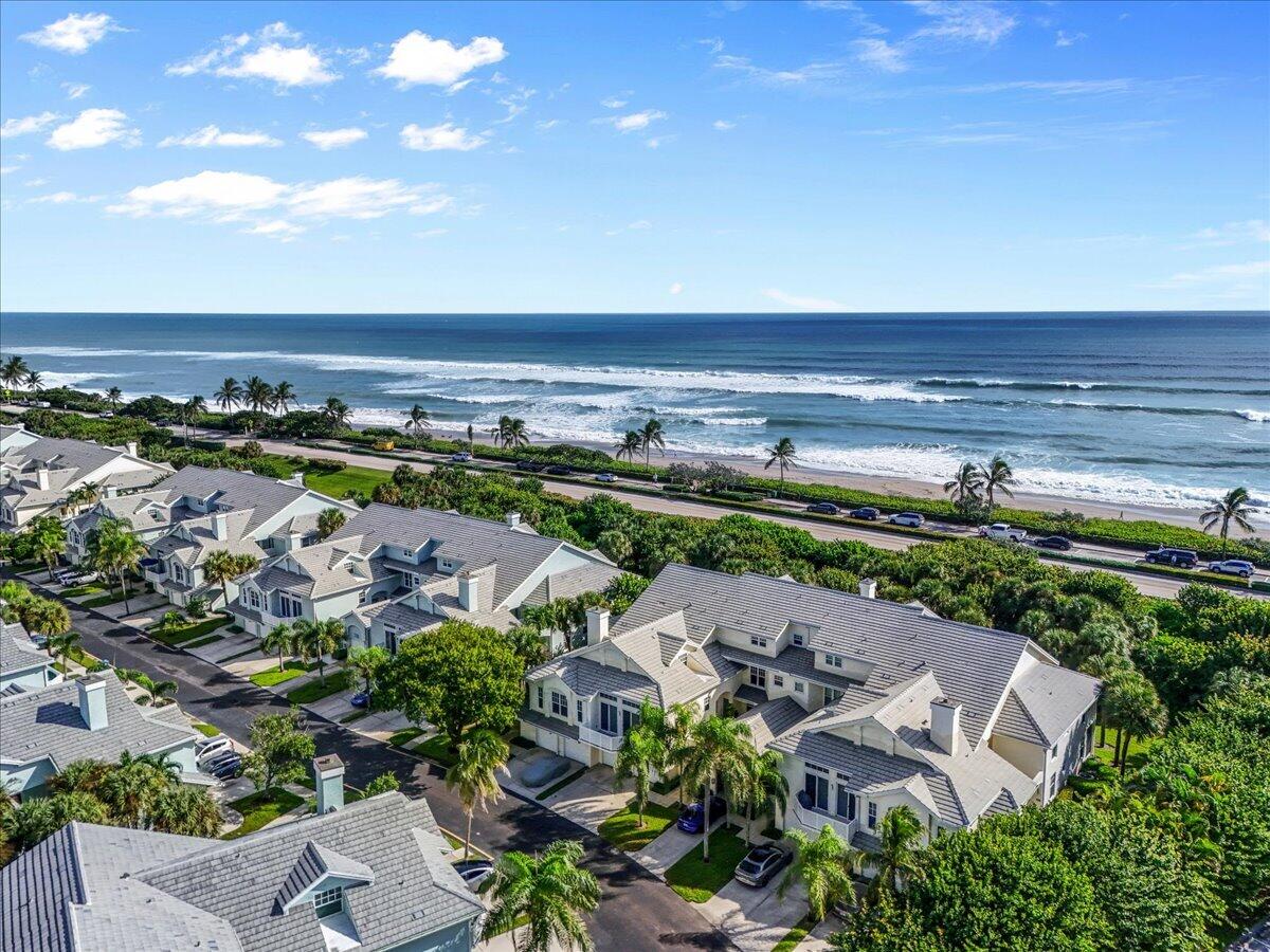 Aerial view of coastal homes beside a palm-lined road, sandy beach, and ocean waves.