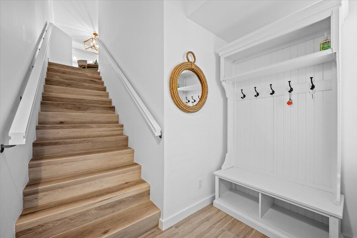 Wood staircase beside a built-in white entry bench with coat hooks and a rope-framed mirror.