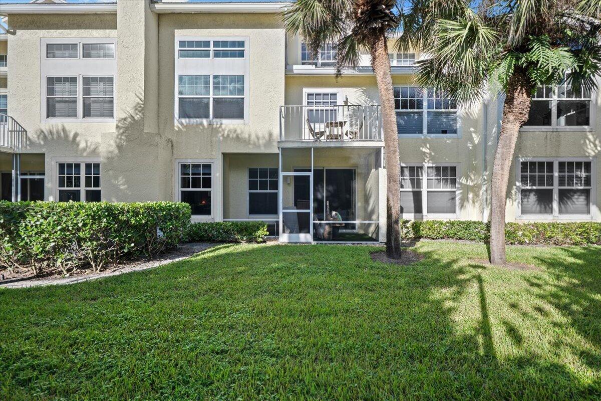 Two-story residence with a balcony and screened patio behind a lawn and palm trees.