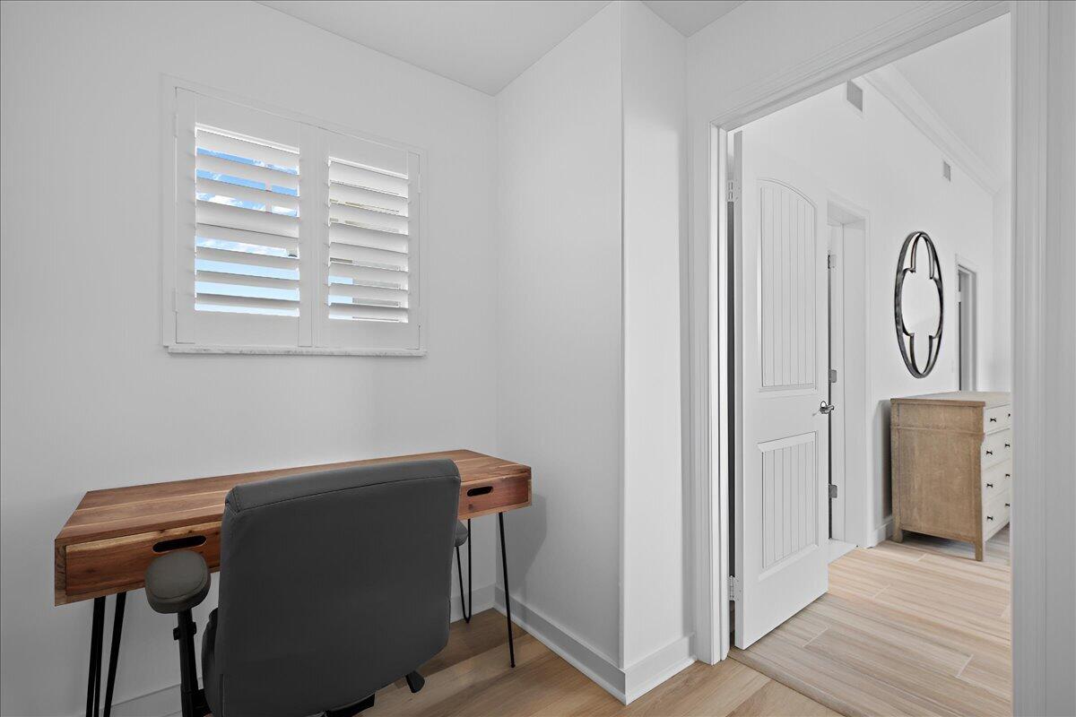Home office nook with a wood desk beneath plantation shutters and an open doorway to the hall.