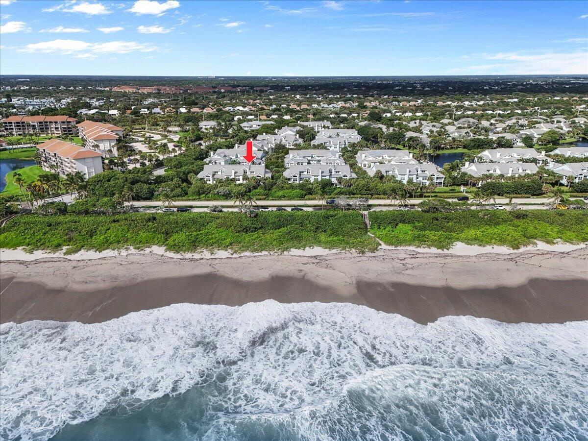 Aerial view of an oceanfront neighborhood, with a red arrow marking a white-roofed home above the beach.