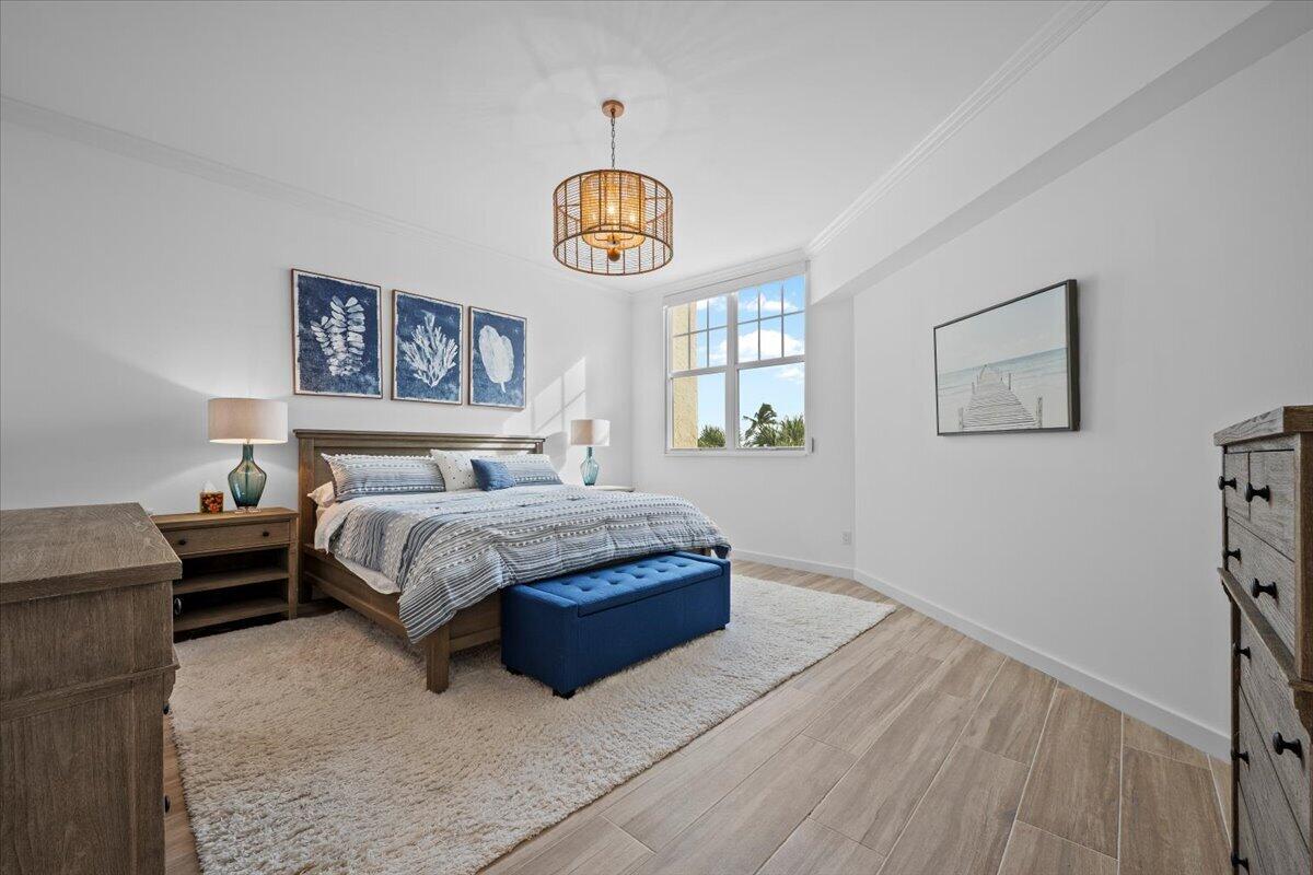 Furnished bedroom with blue-and-white bedding, a blue bench, coastal artwork, and a large window.