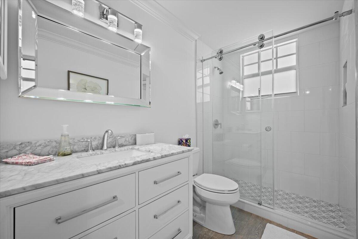 Bathroom with a marble-topped vanity and glass shower with patterned tile floor.
