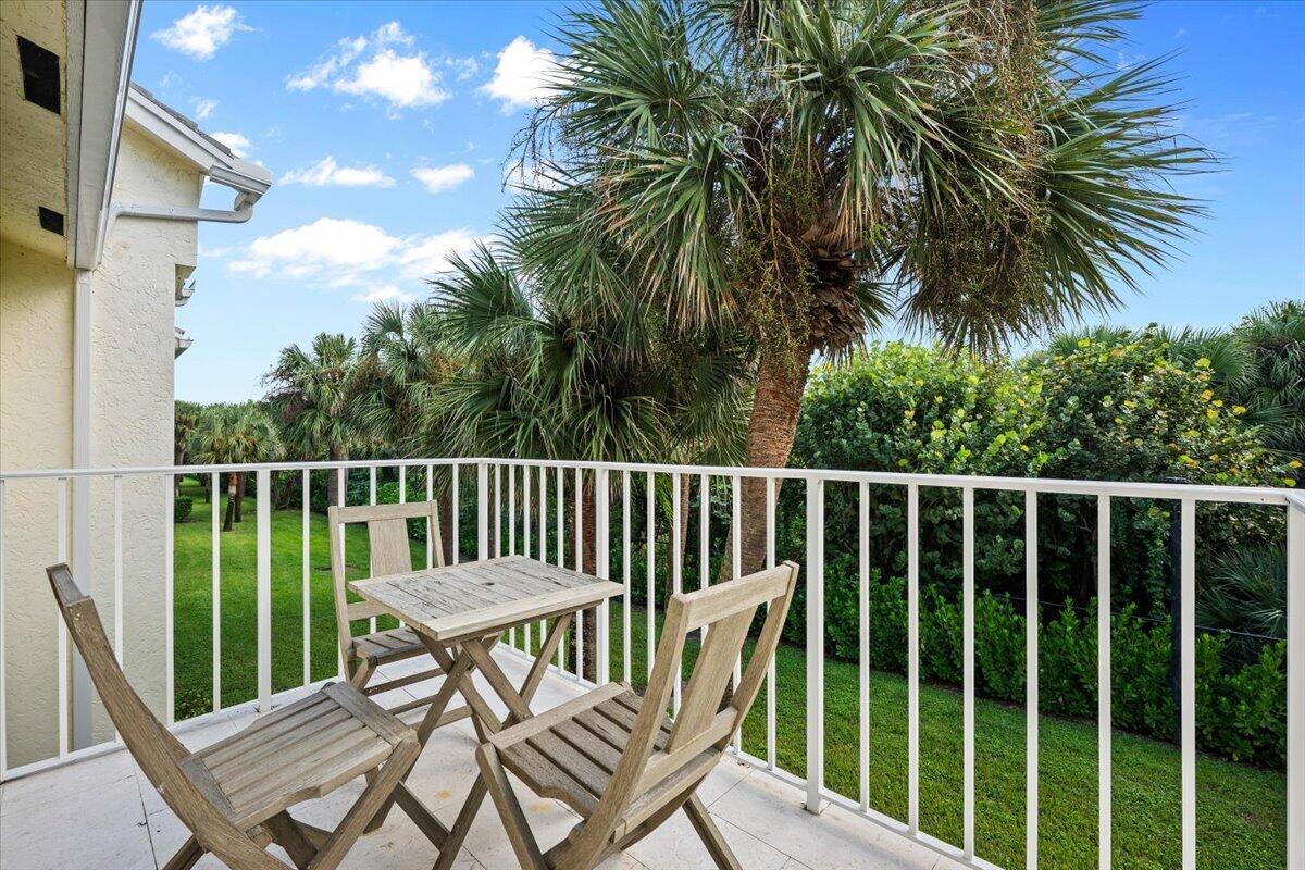 Furnished balcony overlooking a lawn and palm trees, with a wooden table and chairs.